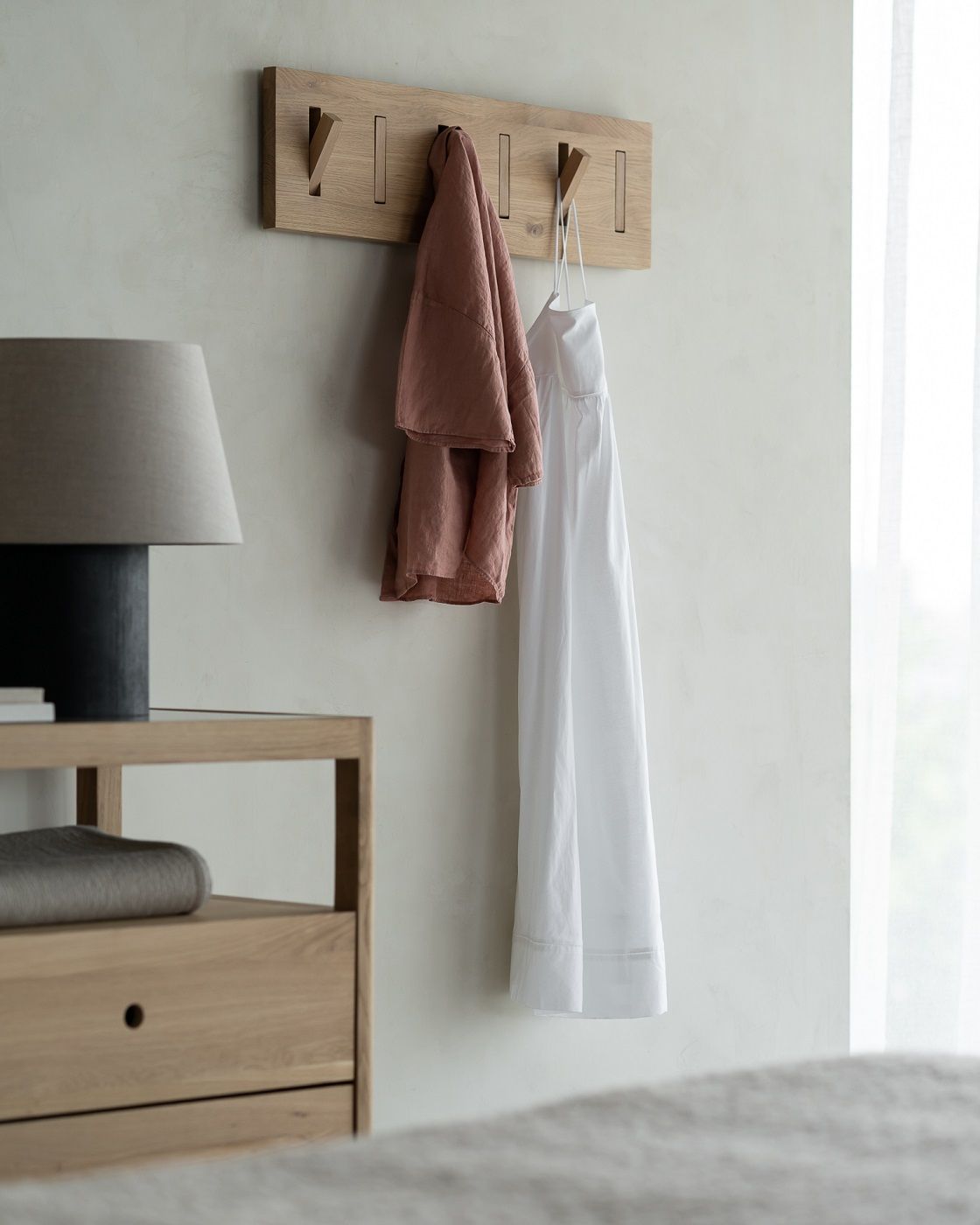 Detailaufnahme einer Ethnicraft Spindle Kommode aus Eiche mit Lampe und Kleiderhaken an der Wand.