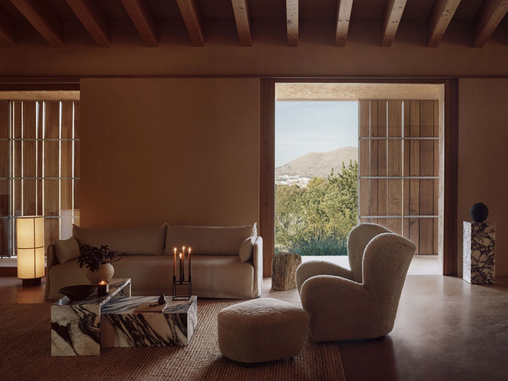 Helles Wohnzimmer mit Audo Copenhagen Offset Sofa, Sessel und Marmor-Couchtisch vor malerischer Landschaft.