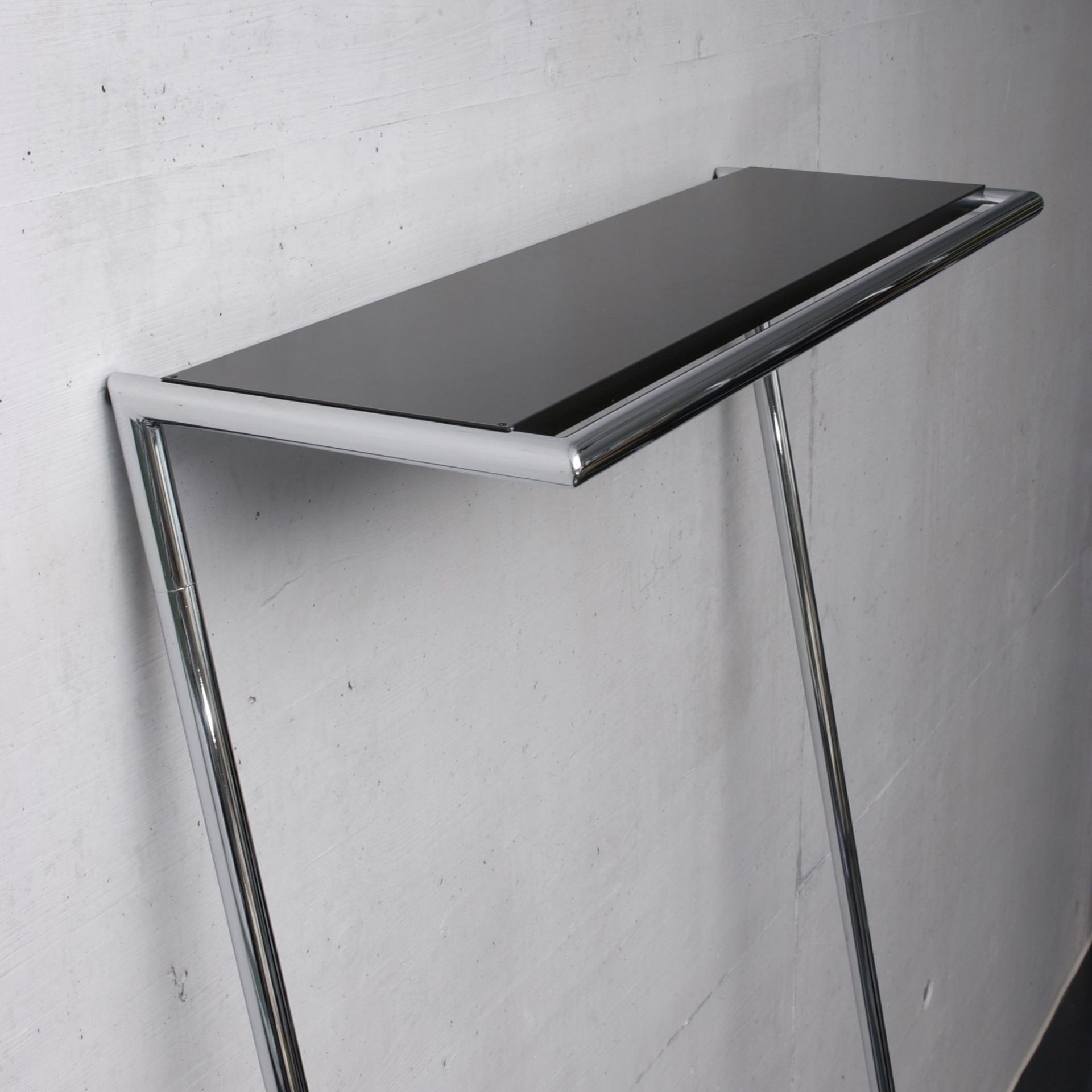 Hutablage für Zen Garderobe: Schwarze Ablage mit verchromtem Gestell vor einer Wand.