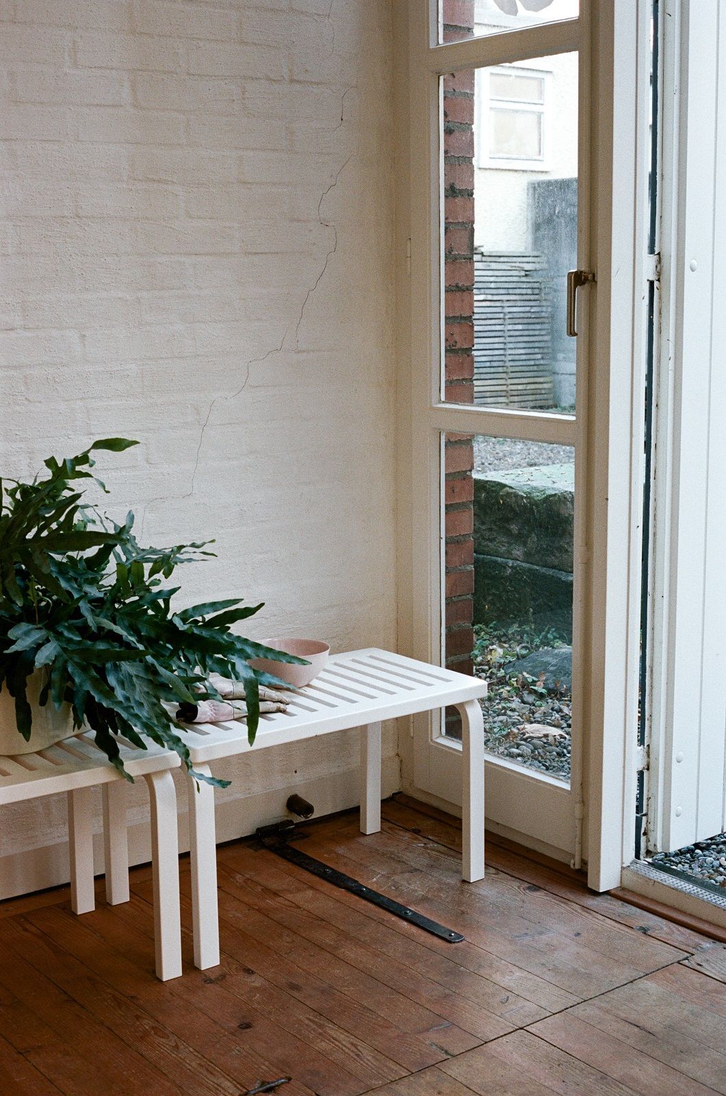 Weiße Artek Bank 153B im minimalistischen Interieur mit Pflanze und Holzboden, ideal als Sitzbank oder Ablage.
