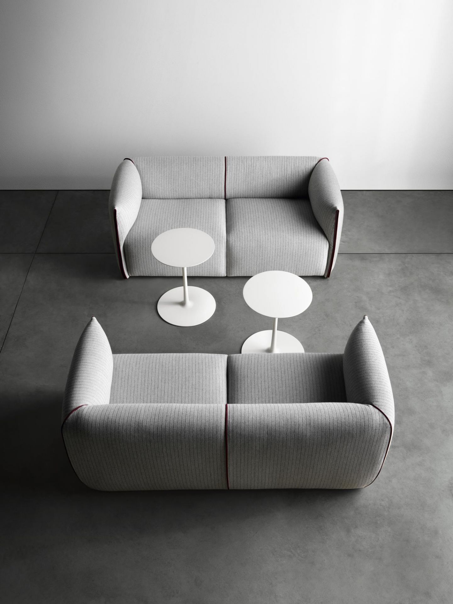 Zwei graue Mia Sofas von MDF Italia mit zwei weißen Tischen auf grauem Untergrund.