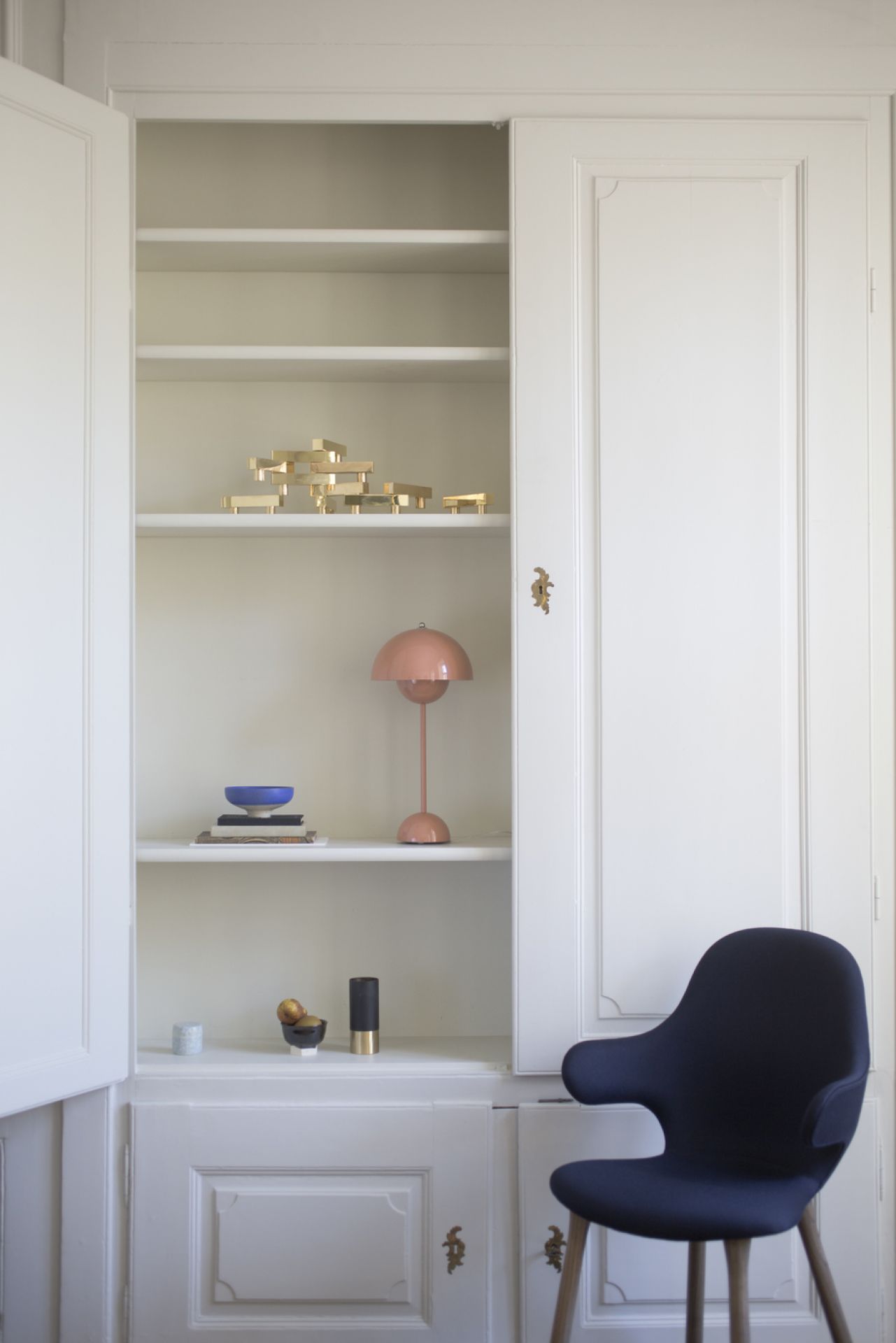 AndTradition Catch Chair JH1 Stuhl in dunklem Blau vor weißem Schrank mit Deko-Elementen.