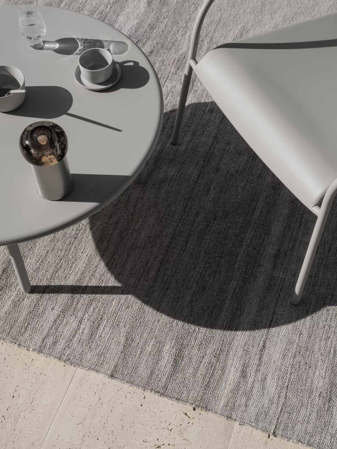 Detailaufnahme: Blomus Kiva Rug Outdoor Teppich in Zink Melange unter Tisch und Stuhl.