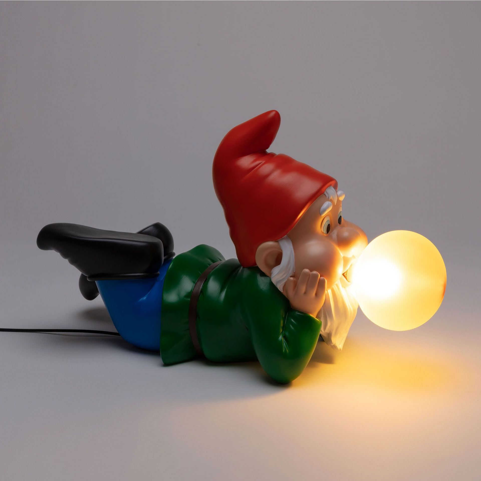 Seletti Gummy Dreaming Leuchte: Liegender Gartenzwerg mit roter Mütze und leuchtender Kugel als Lampe.
