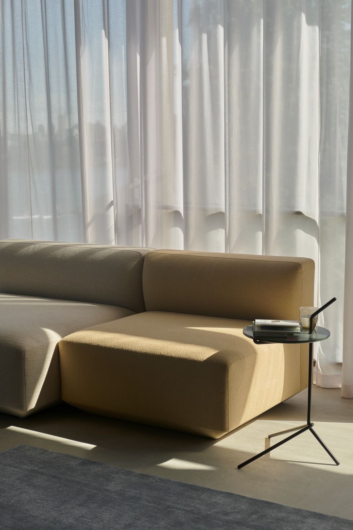 AndTradition Halten Beistelltisch SH9 neben Sofa mit Getränk und Büchern im hellen Raum.