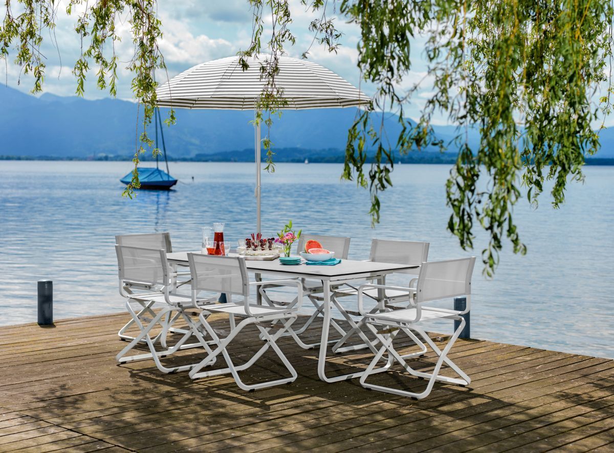 Ahoi Sessel Outdoor Weishäupl: Weißer Gartensessel mit Tisch und Sonnenschirm am See. Gartenmöbel für Terrasse.