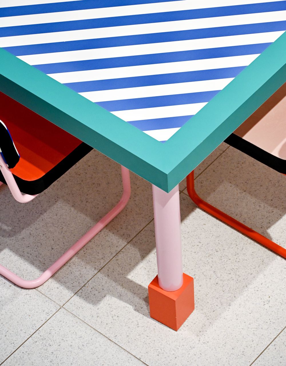 Detailaufnahme des Seletti Supersquare Table Esstischs mit blau-weiß gestreifter Tischplatte und farbenfrohen Tischbeinen.