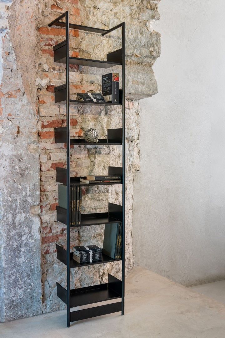 Schwarzes Pool Anlehnregal von Mox, Medium, vor einer Backsteinwand, mit Büchern und Dekoartikeln.
