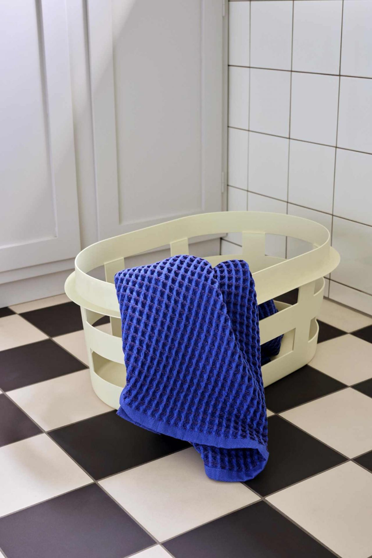 Blauer Frottee-Waschlappen liegt in einem hellen Hay Wäschekorb S RECYCLED auf Schachbrettboden.