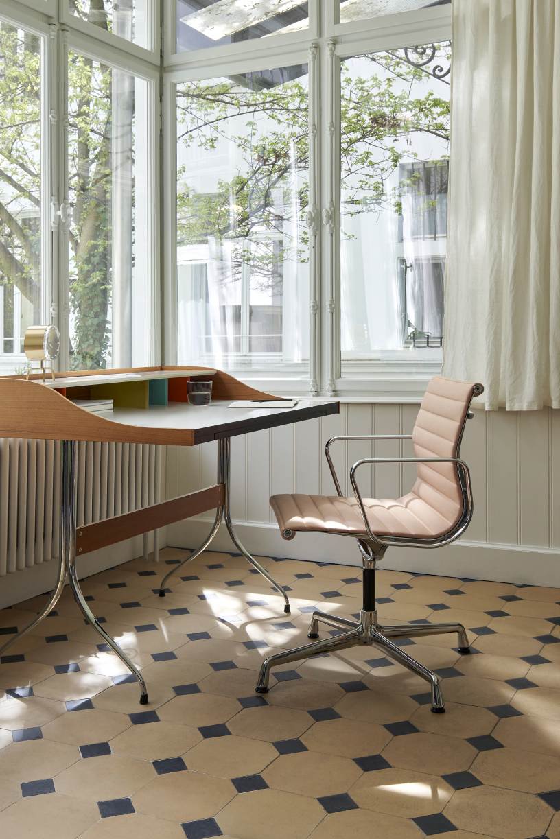Büro mit Schreibtisch, Bürostuhl und Tripod Clock Tischuhr von Vitra vor einem Fenster.