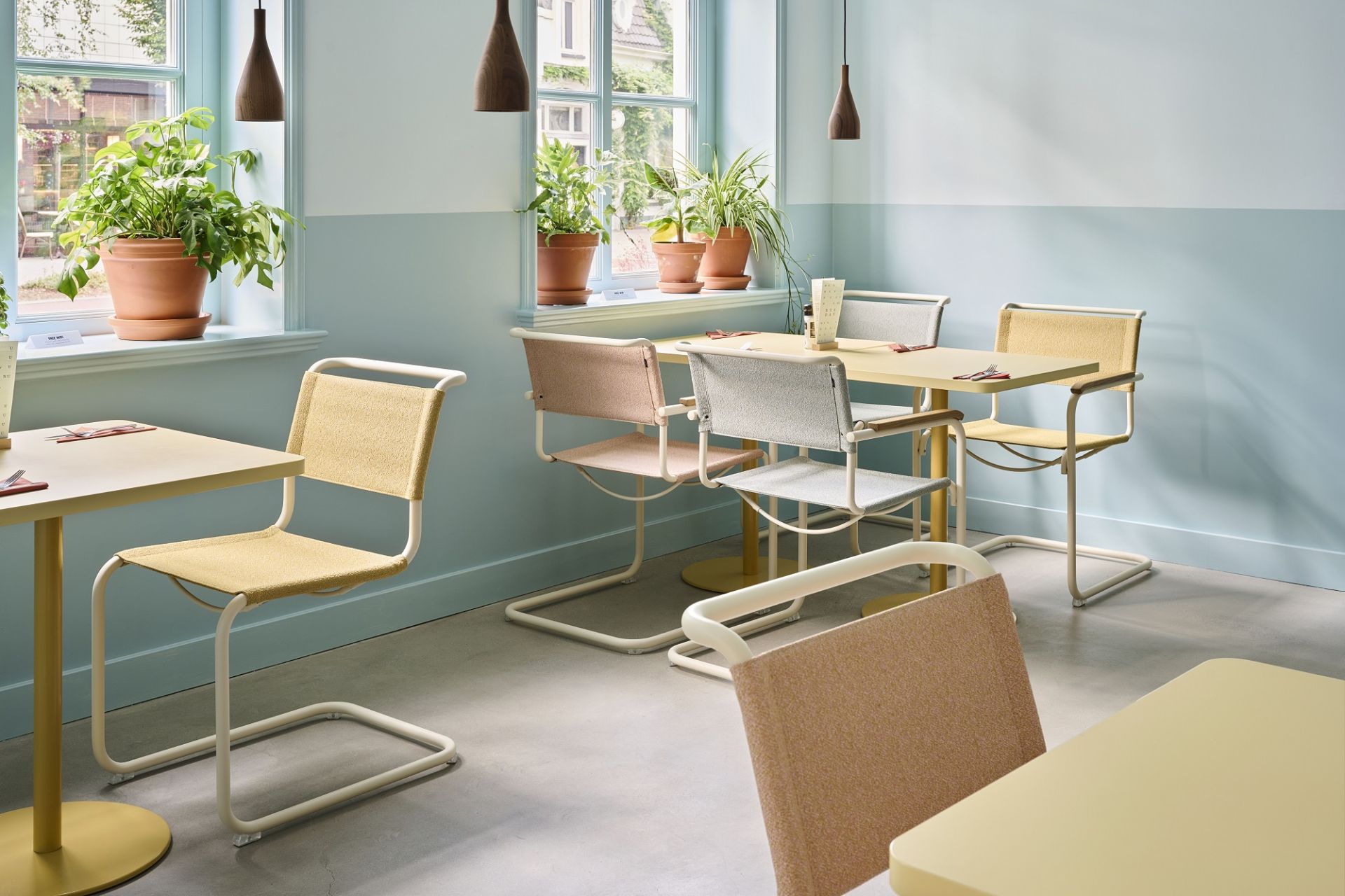 Innenaufnahme eines Restaurants mit mehreren Thonet S 34 Freischwinger Stühlen in verschiedenen Farben an gelben Tischen.