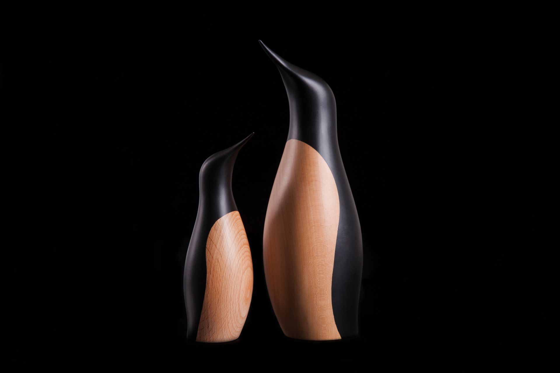 Zwei Pinguin Holzfiguren von Architectmade, eine kleine und eine große, auf schwarzem Hintergrund.