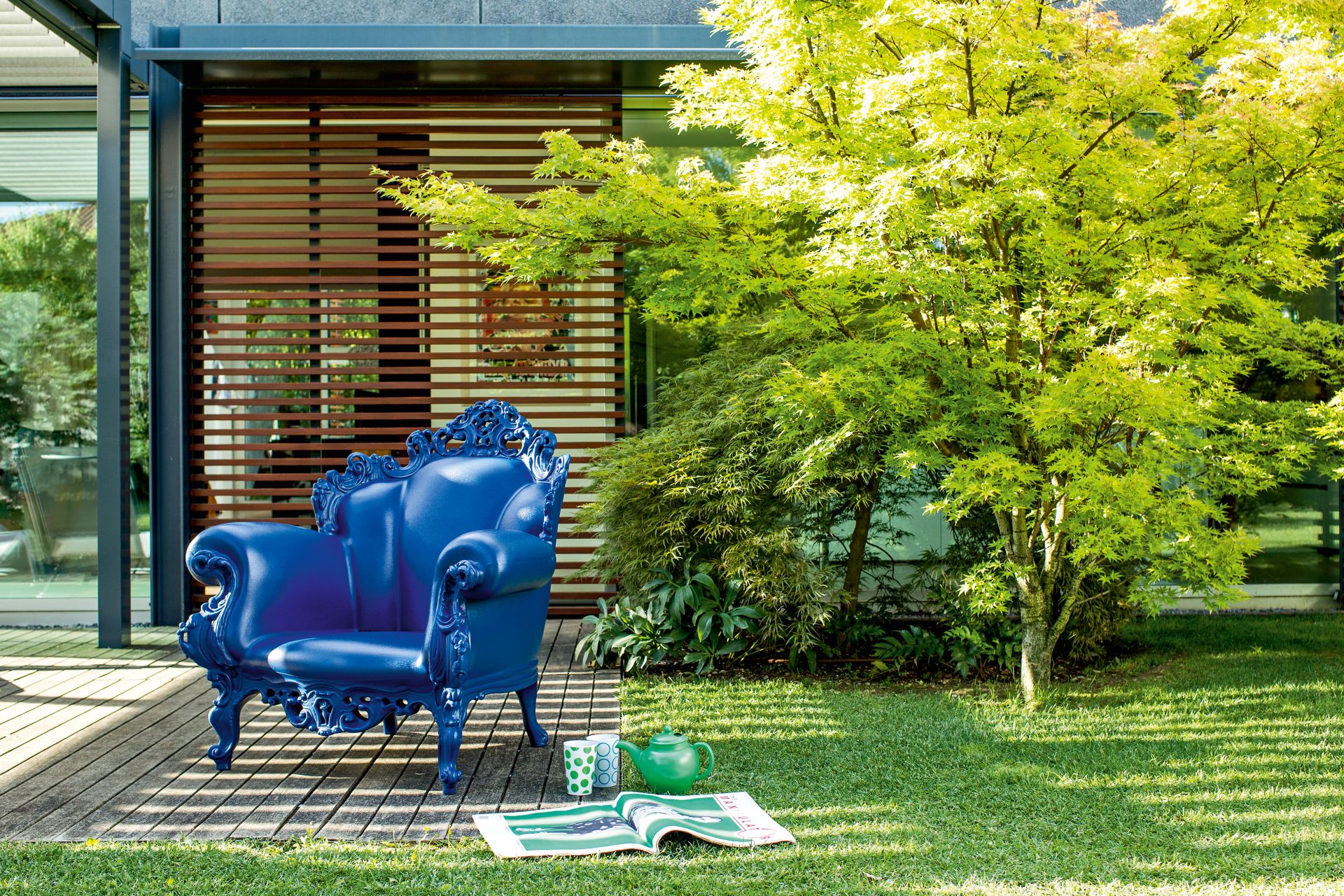 Blauer Magis Proust Sessel Outdoor auf Holzterrasse vor modernem Haus und Garten.