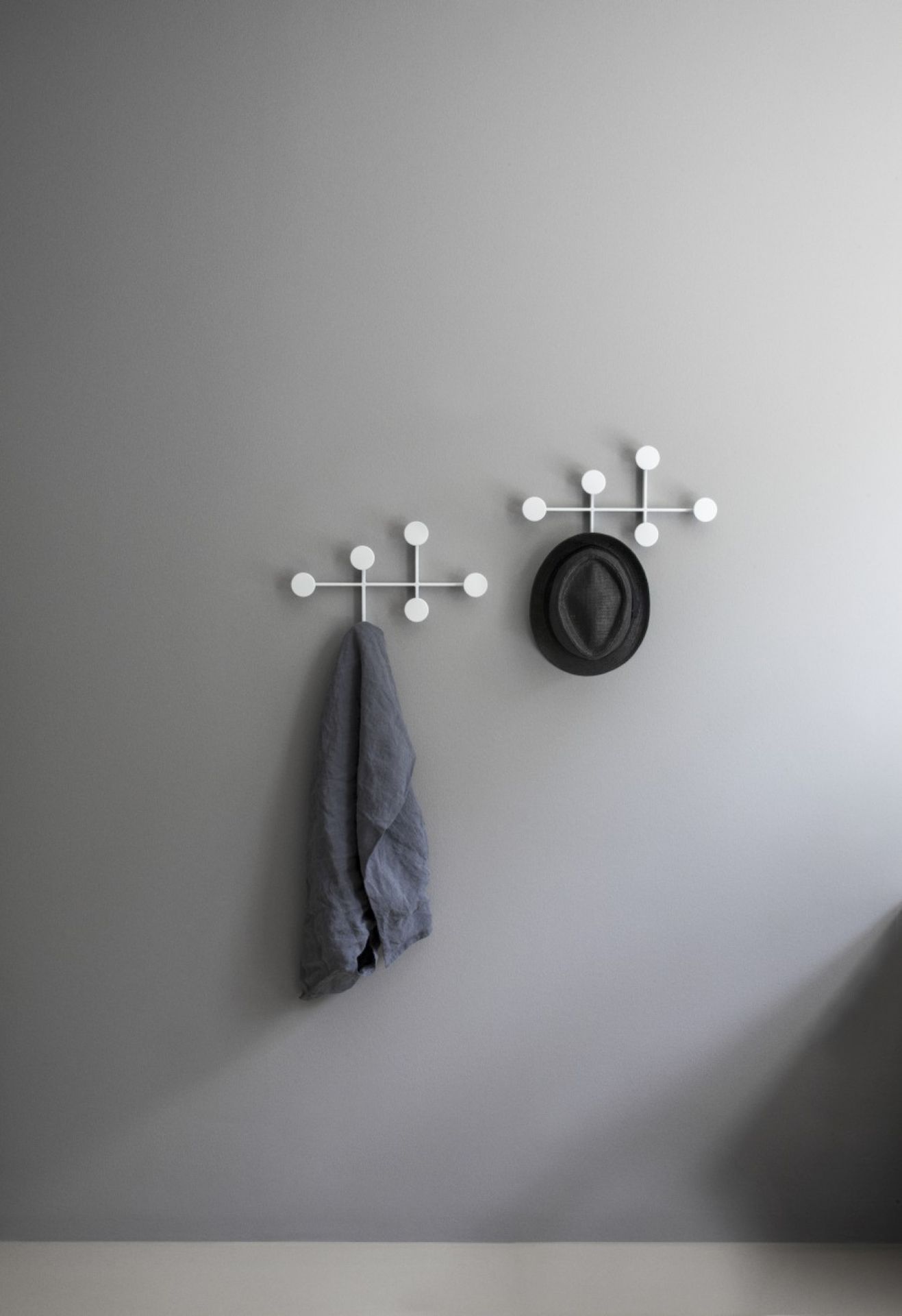 Afteroom Coat Hanger Medium: Zwei weiße Garderobenhaken mit Tuch und Hut an grauer Wand.
