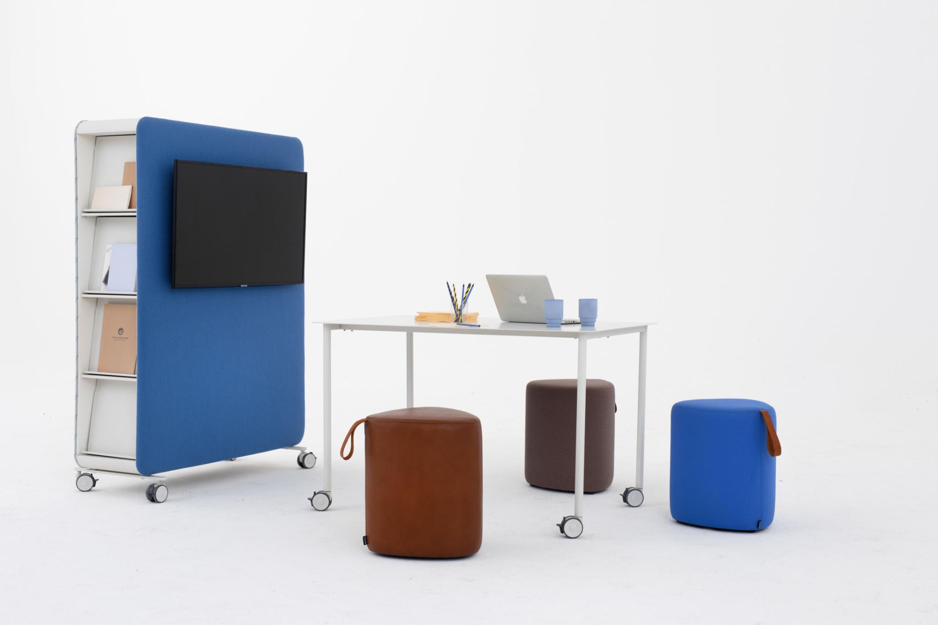 Büro mit Cascando Pillow Space Akustik-Raumteiler in Blau, weißem Tisch, Laptop und farbigen Hockern auf Rollen.