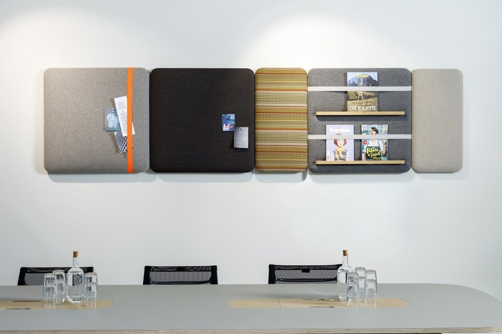 Cascando Pillow Wall Pinnwände: Modulare Wandpaneele in Grau, Schwarz und mit Regalen für Zeitschriften.