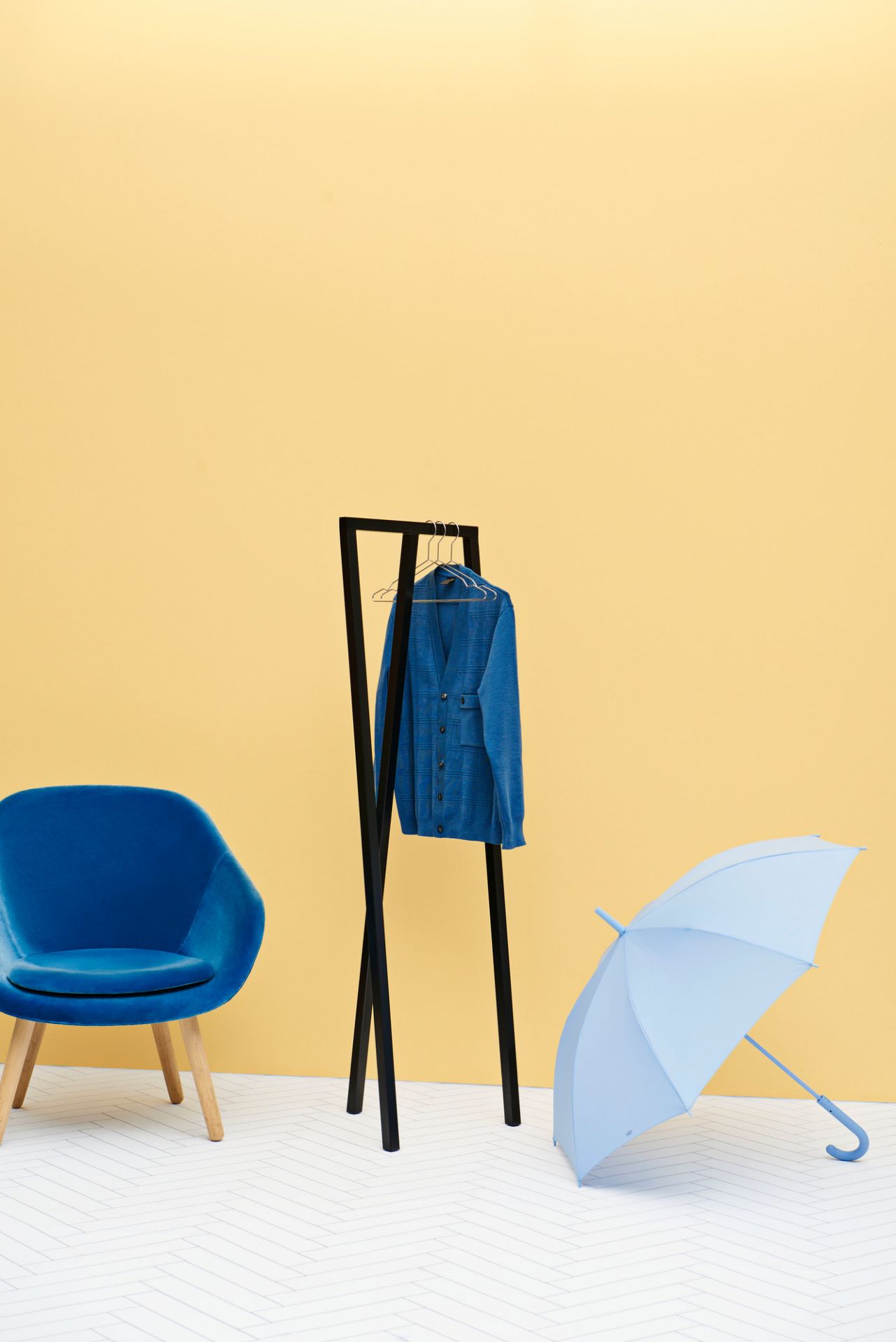 Blauer About a Lounge AAL 82 Sessel von Hay mit Jacke und Schirm vor gelbem Hintergrund.