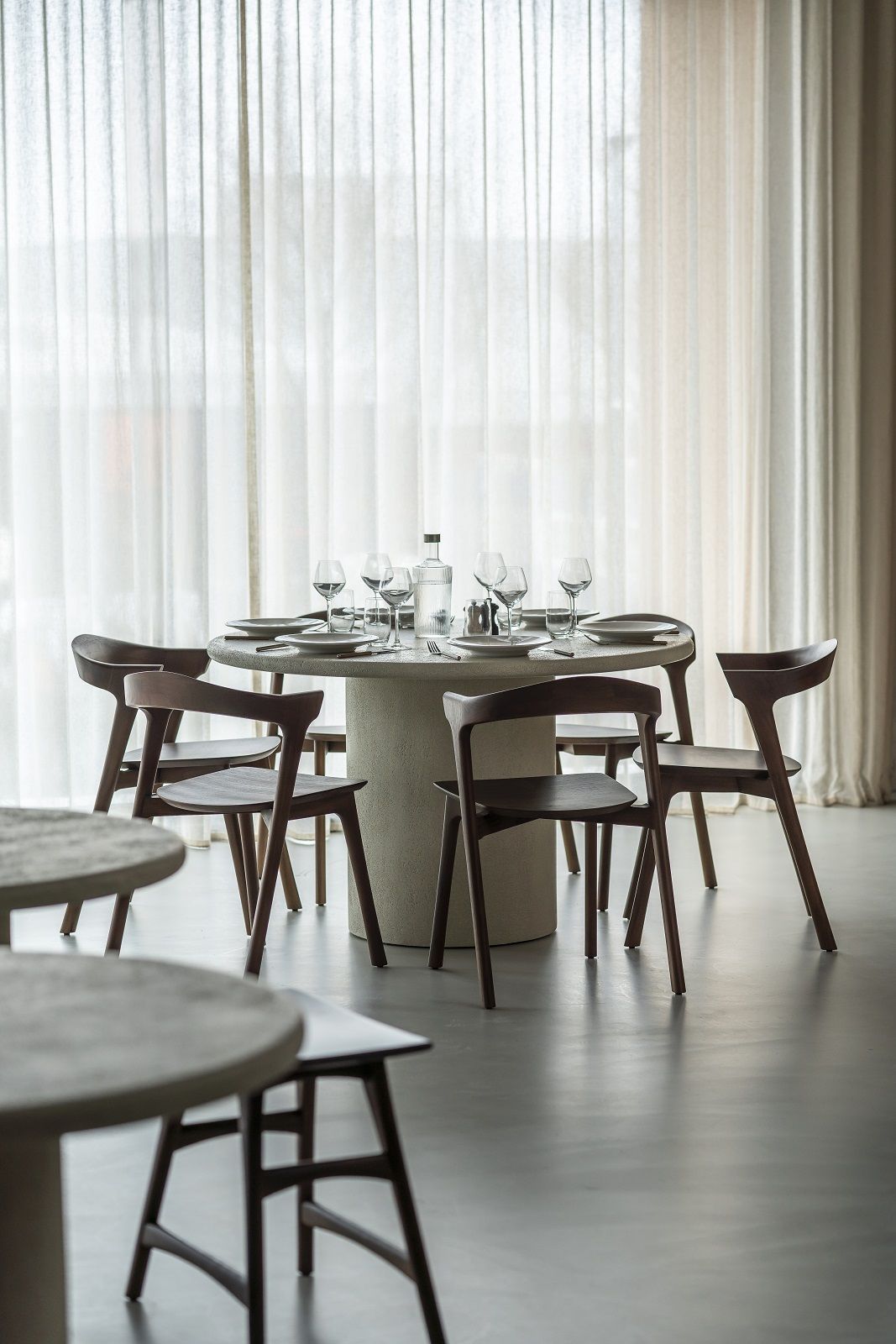 Elements Dining Table Esstisch Rund von Ethnicraft mit Stühlen und gedecktem Tisch vor hellem Vorhang.