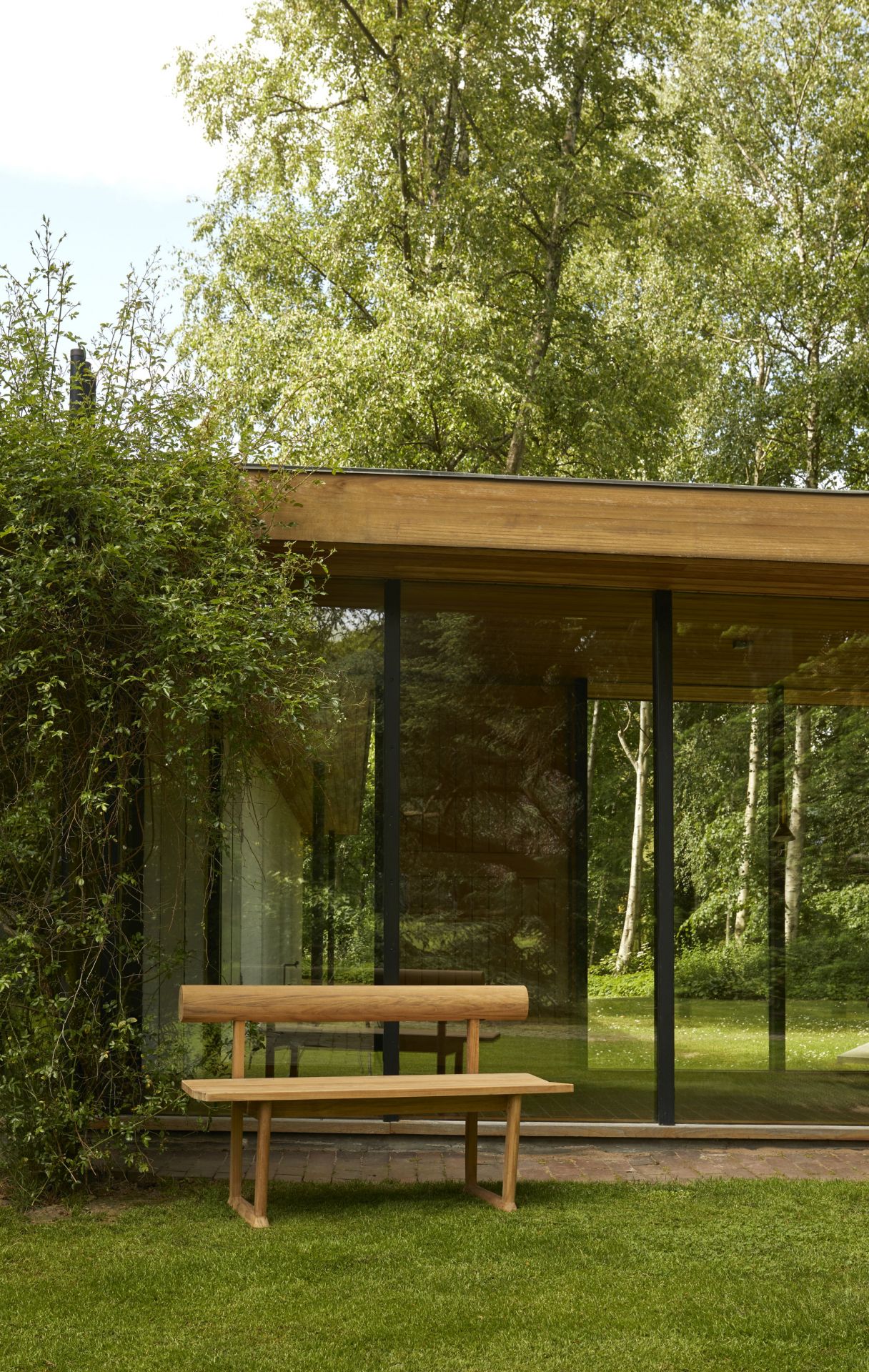 Banco Bank Teak Outdoor von Skagerak by Fritz Hansen vor einem modernen Haus mit Glasfassade.