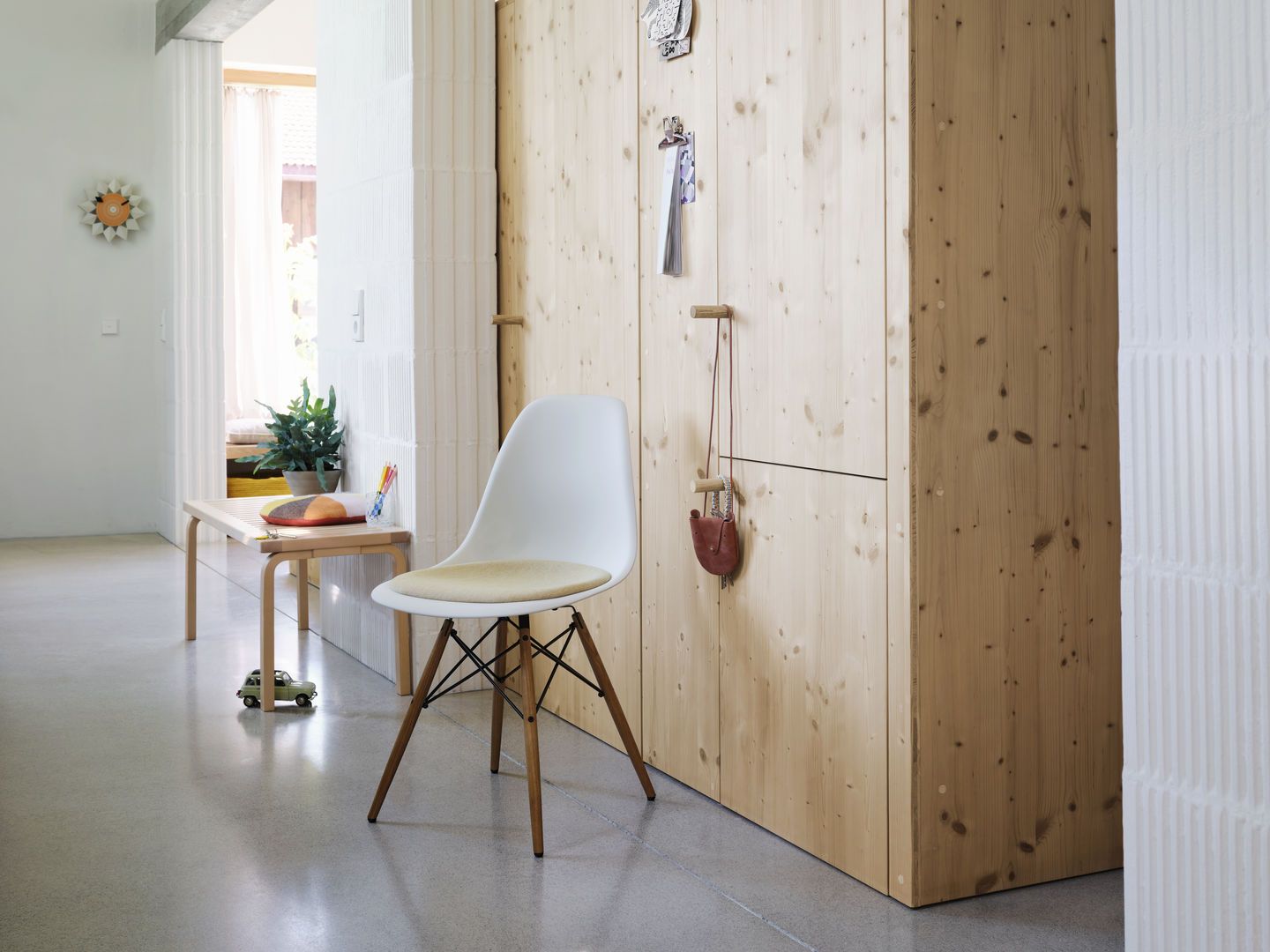 Weißer Eames Plastic Side Chair DSW Stuhl von Vitra mit Holzbeinen und beigem Sitzkissen im Flur.