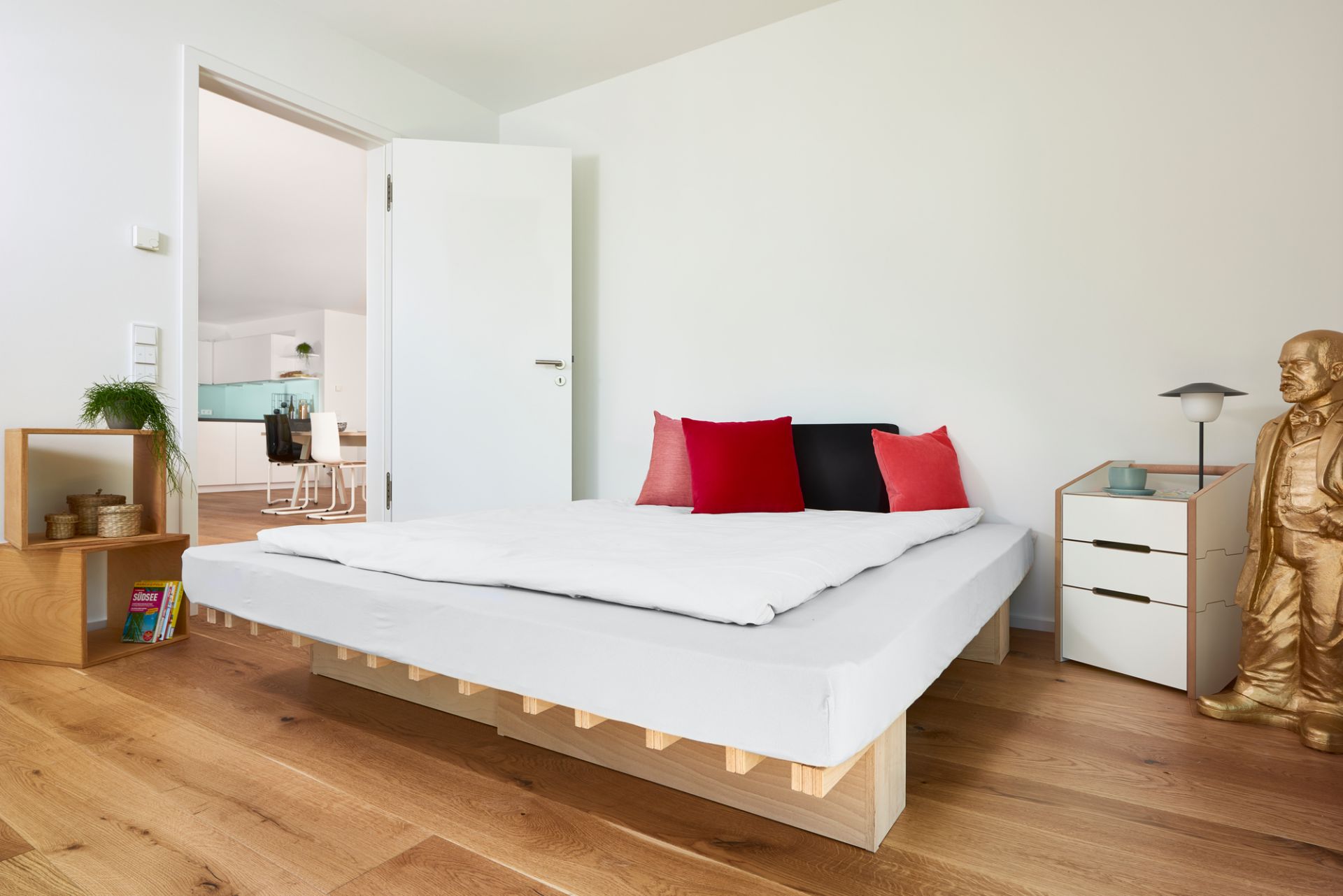 Tojo Ergo Faltmatratze im Schlafzimmer mit weißer Bettwäsche und farbigen Kissen auf Holzboden.