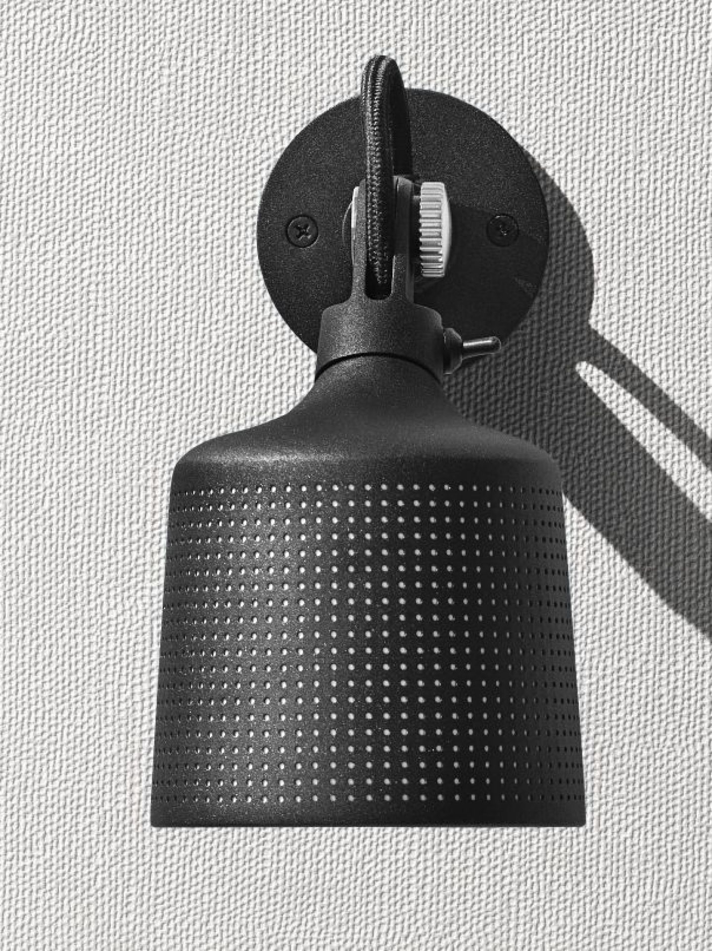 Schwarzer Vipp Wandspot mit perforiertem Schirm und Textilkabel an einer weißen Wand, Nahaufnahme für E-Commerce.