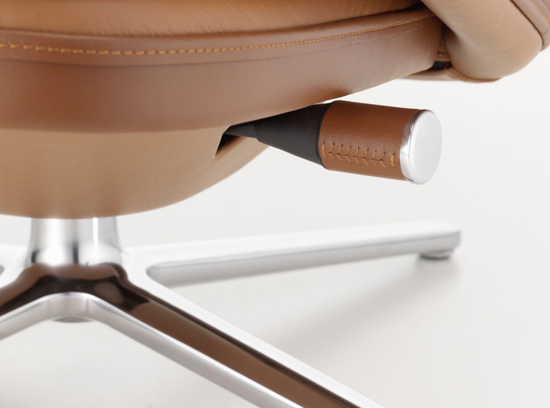 Detailaufnahme: Verstellhebel und Fußkreuz des Vitra Grand Relax Sessels in braunem Leder und Aluminium.