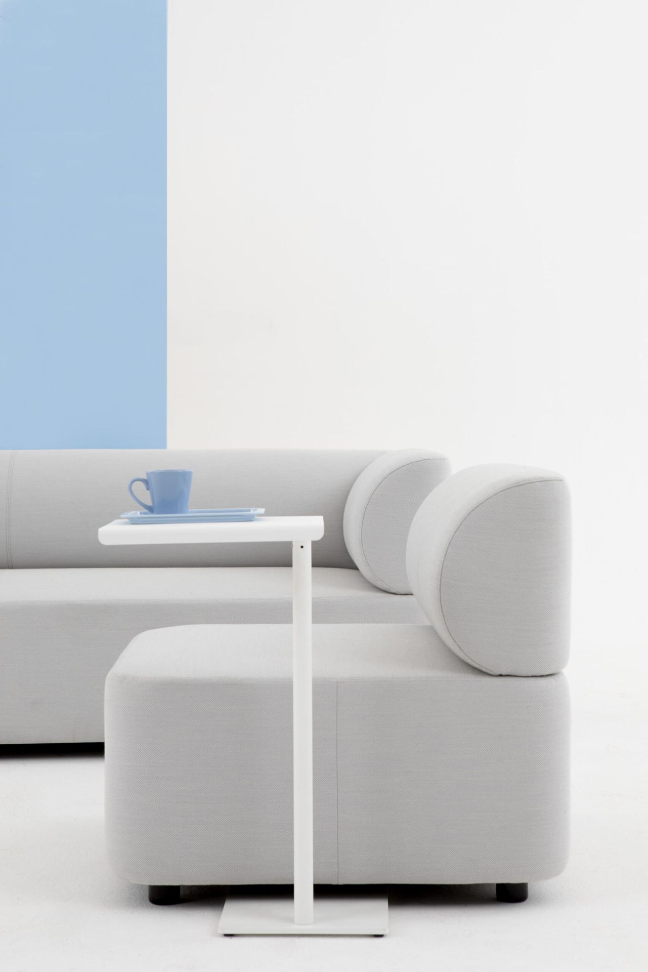 Mezza Sitzelement Sofa von Cascando in hellgrau mit Beistelltisch und blauer Tasse.