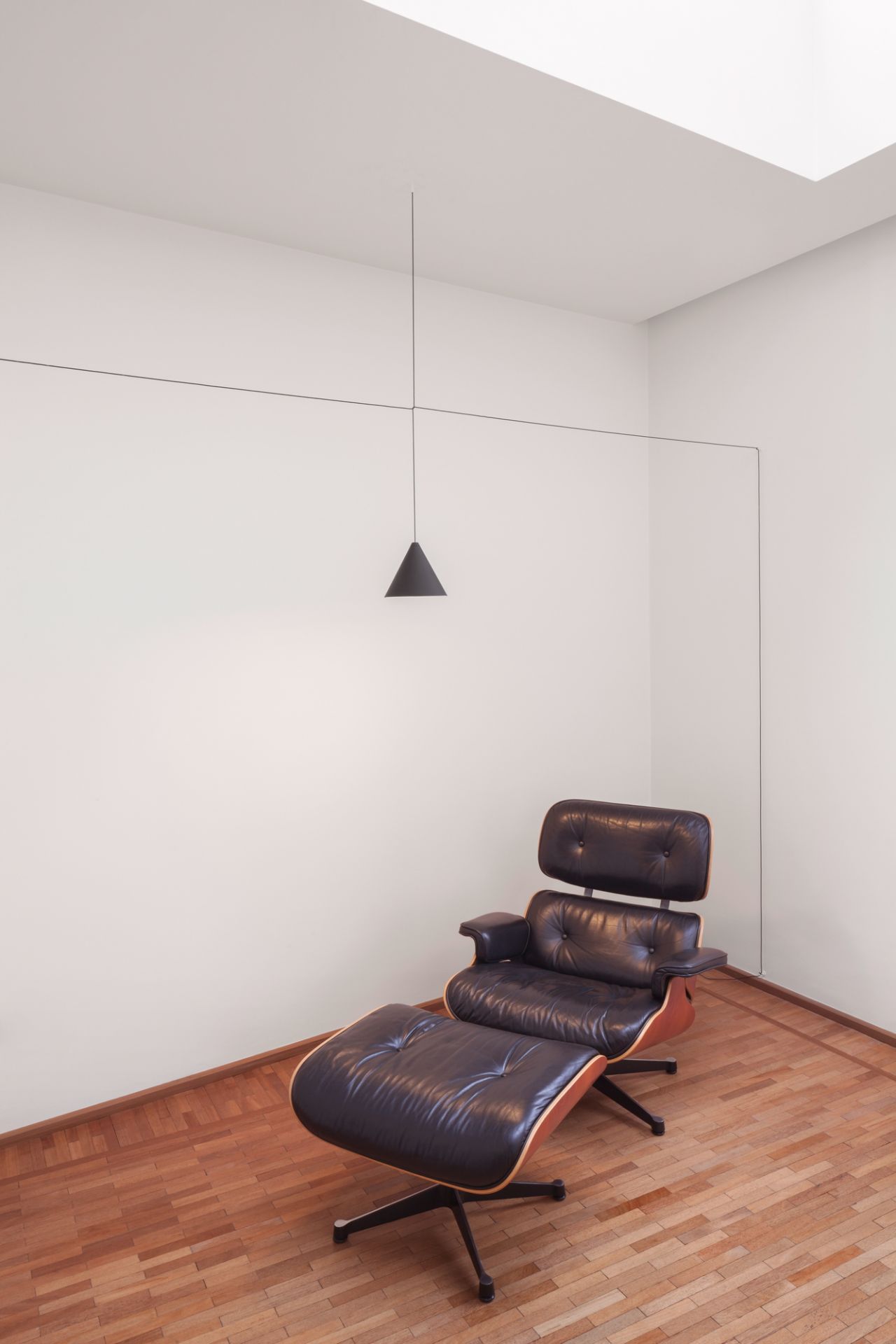 Minimalistische Raumgestaltung mit Flos String Light Kegelkopf Pendelleuchte über Ledersessel. Design Lampe für Wohnzimmer.
