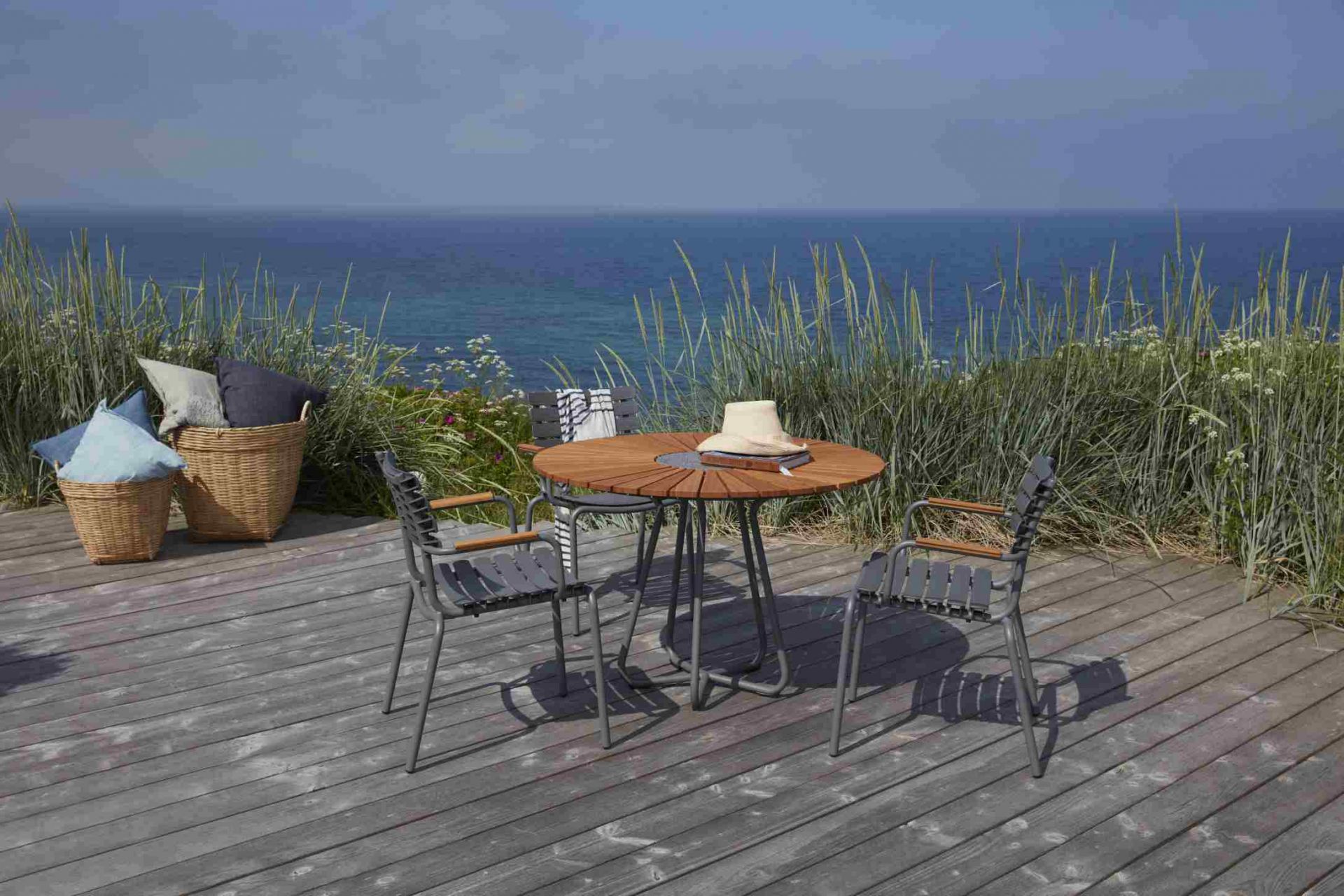 Houe Circle Gartentisch Ø 110 cm aus Bambus mit grauen Stühlen auf Holzterrasse am Meer.