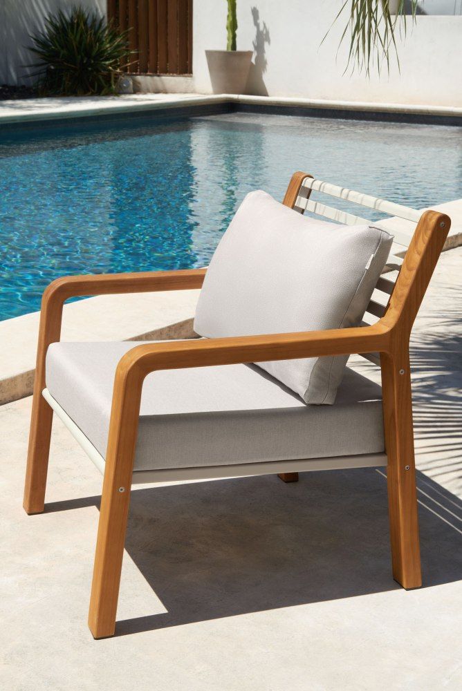 Fermob Somerset Outdoor Sessel mit hellgrauen Polstern und Holzrahmen am Pool.