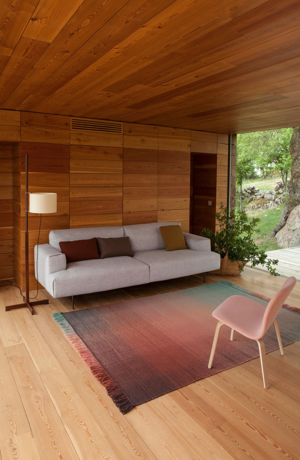 Nanimarquina Shade Teppich im Innenraum mit Sofa, Stuhl und Holzwand für gemütliches Wohnen.