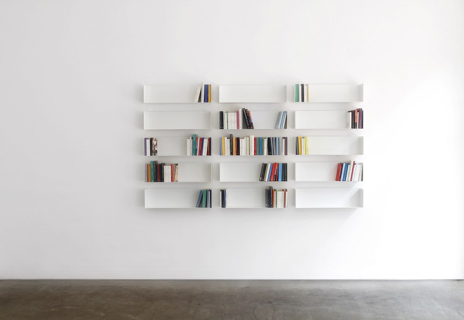 Weißes Taschenbuchregal a Linea1 von Müller Möbelwerkstätten an einer weißen Wand mit Büchern.