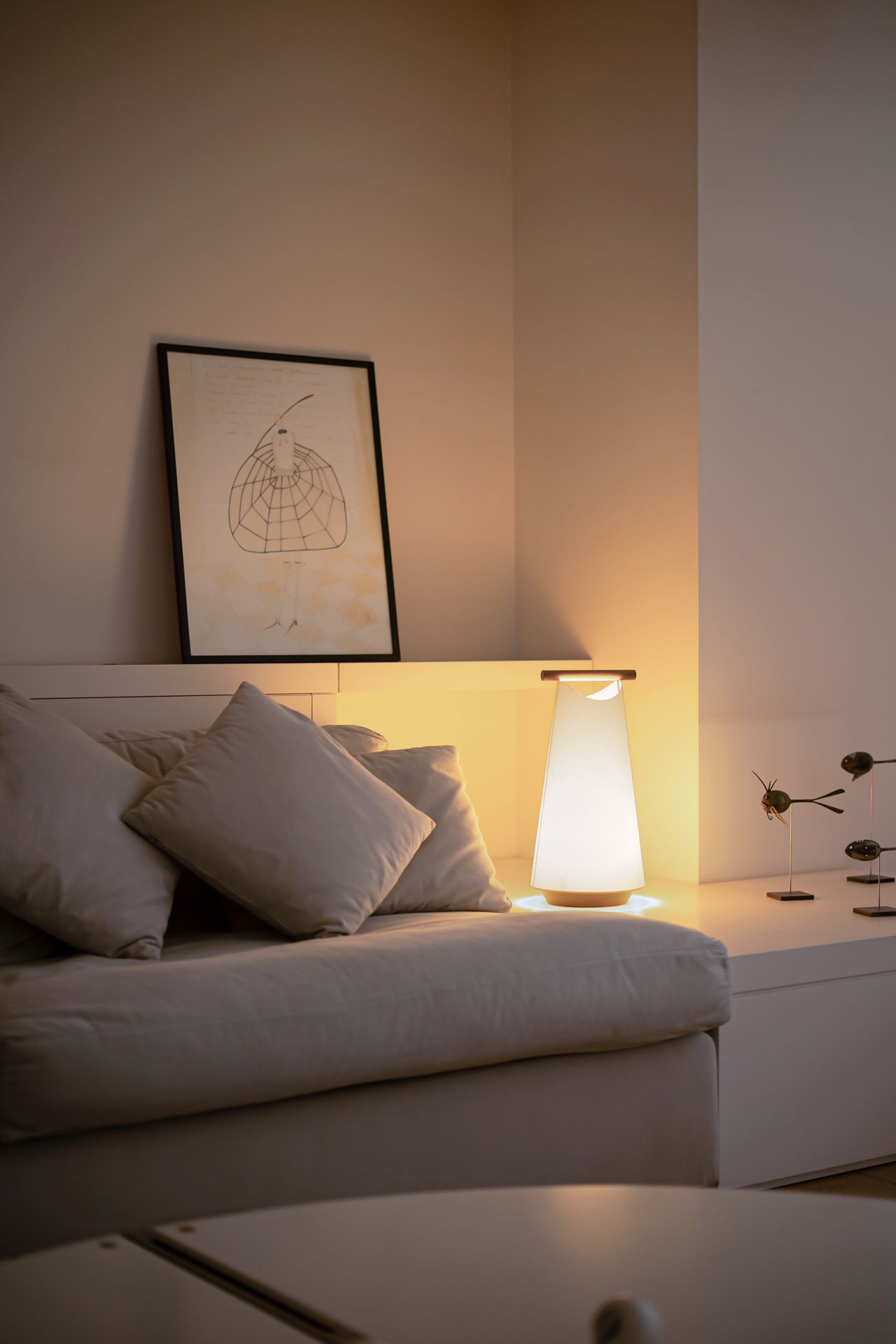 Nomon Catay Tischleuchte aus Holz und Stoff, warmes Licht neben Sofa im Wohnzimmer.