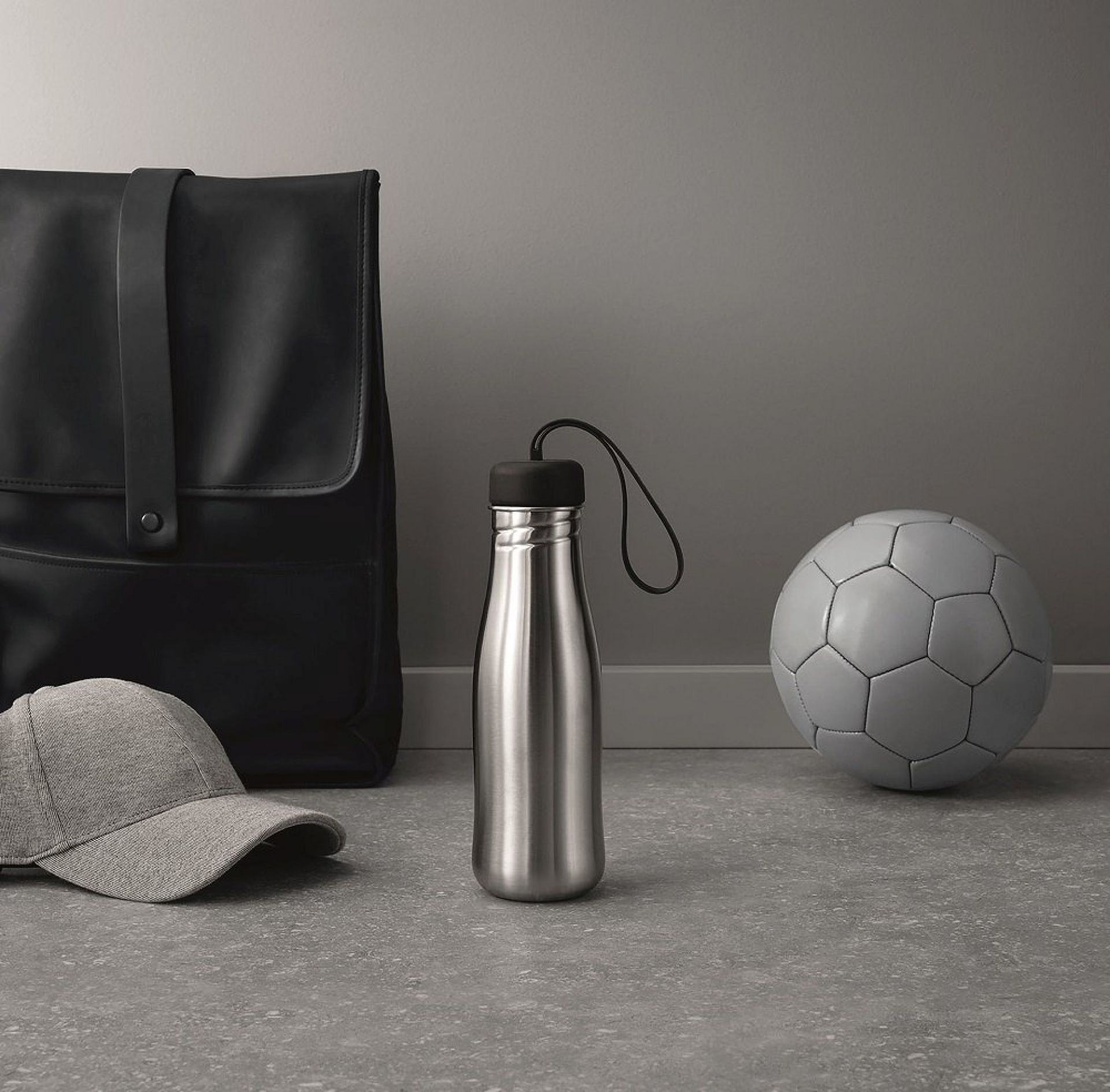 Edelstahl Trinkflasche mit schwarzem Deckel, Active Drinking bottle, neben Rucksack, Kappe und Fußball.