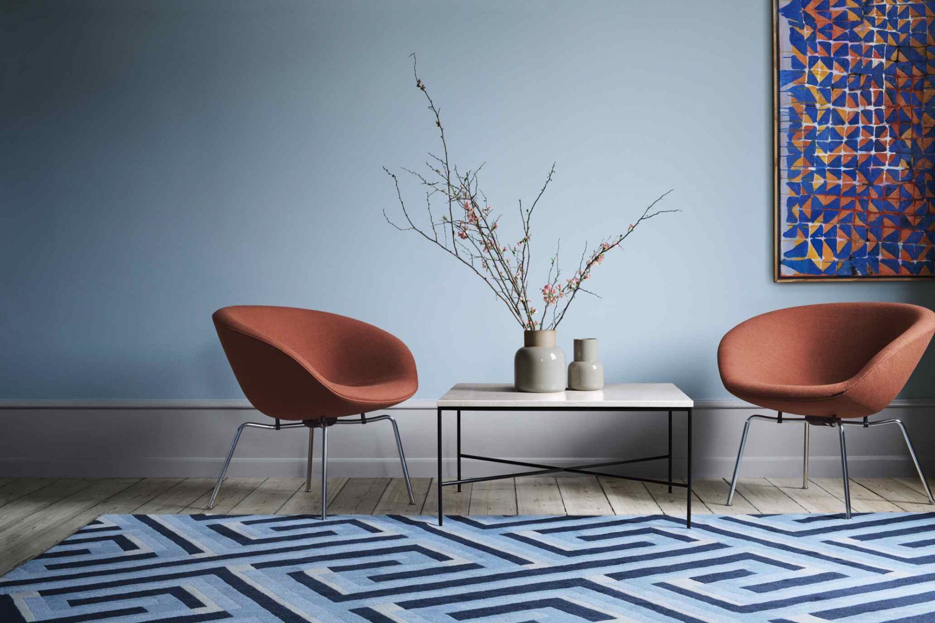 Zwei Fritz Hansen Pot Sessel in Terrakotta mit Couchtisch und blauem Teppich in modernem Wohnzimmer.
