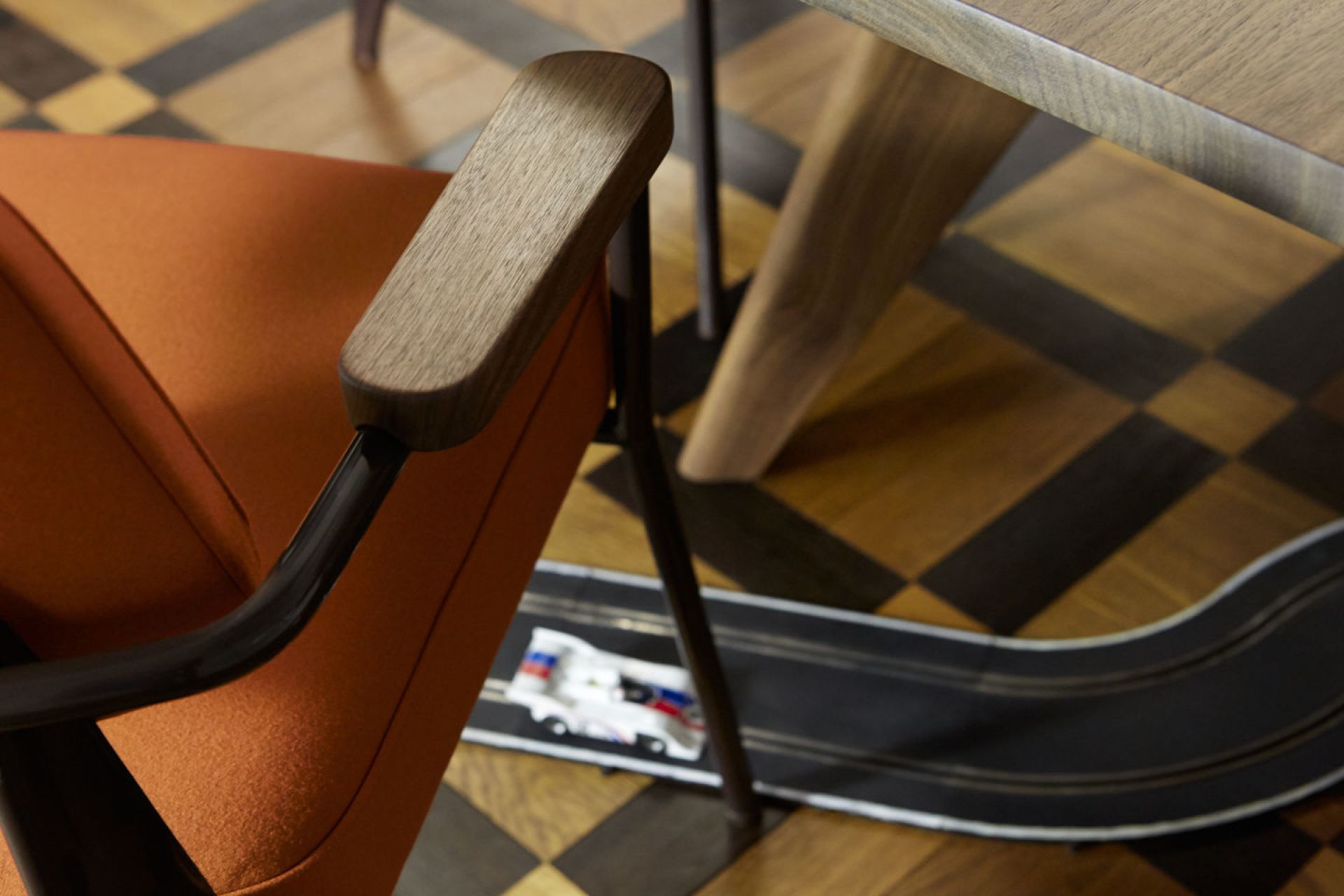 Detailaufnahme vom Fauteuil Direction Sessel von Vitra mit orangefarbenem Bezug und Armlehnen aus Holz.