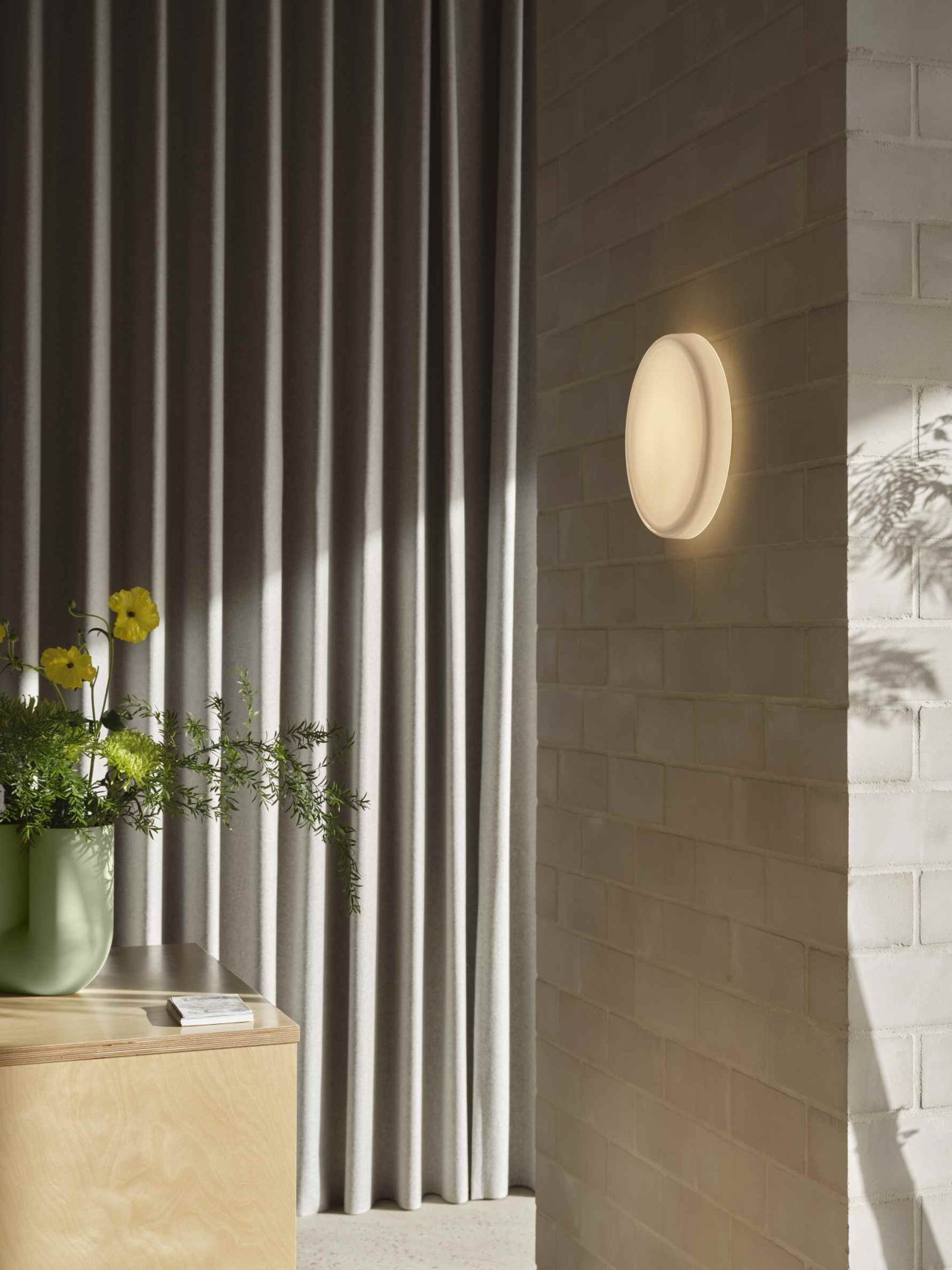 Helle Muuto Looped Wandleuchte an weißer Ziegelwand, indirektes Licht, minimalistisches Design für Wohnraum.