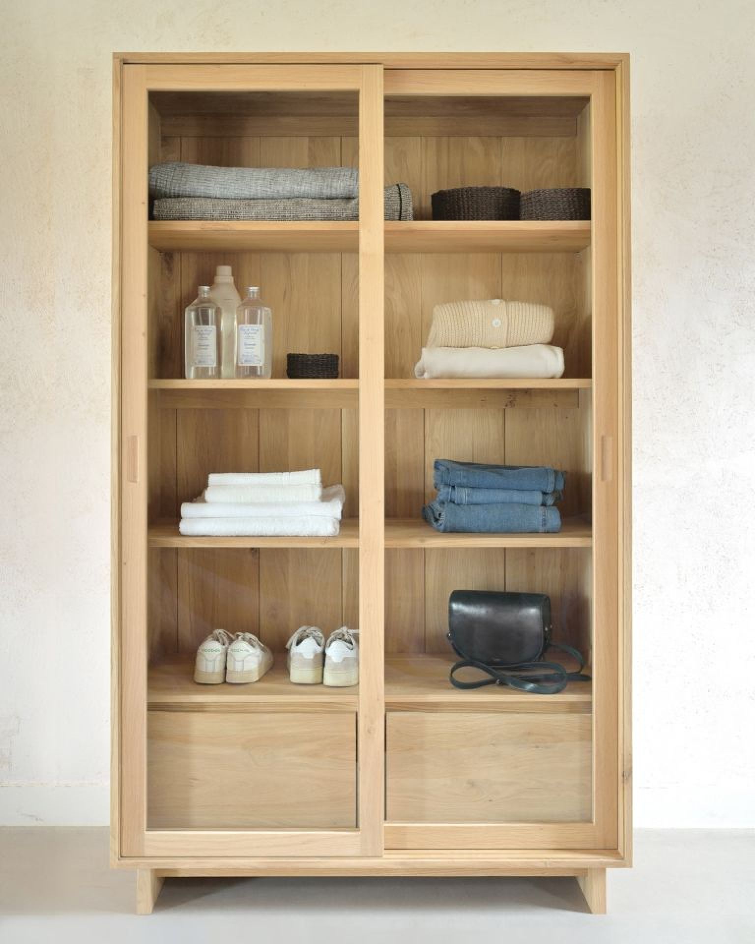 Wave Bücherregal aus Eiche von Ethnicraft mit Schiebetüren, gefüllt mit Kleidung, Handtüchern und Accessoires.