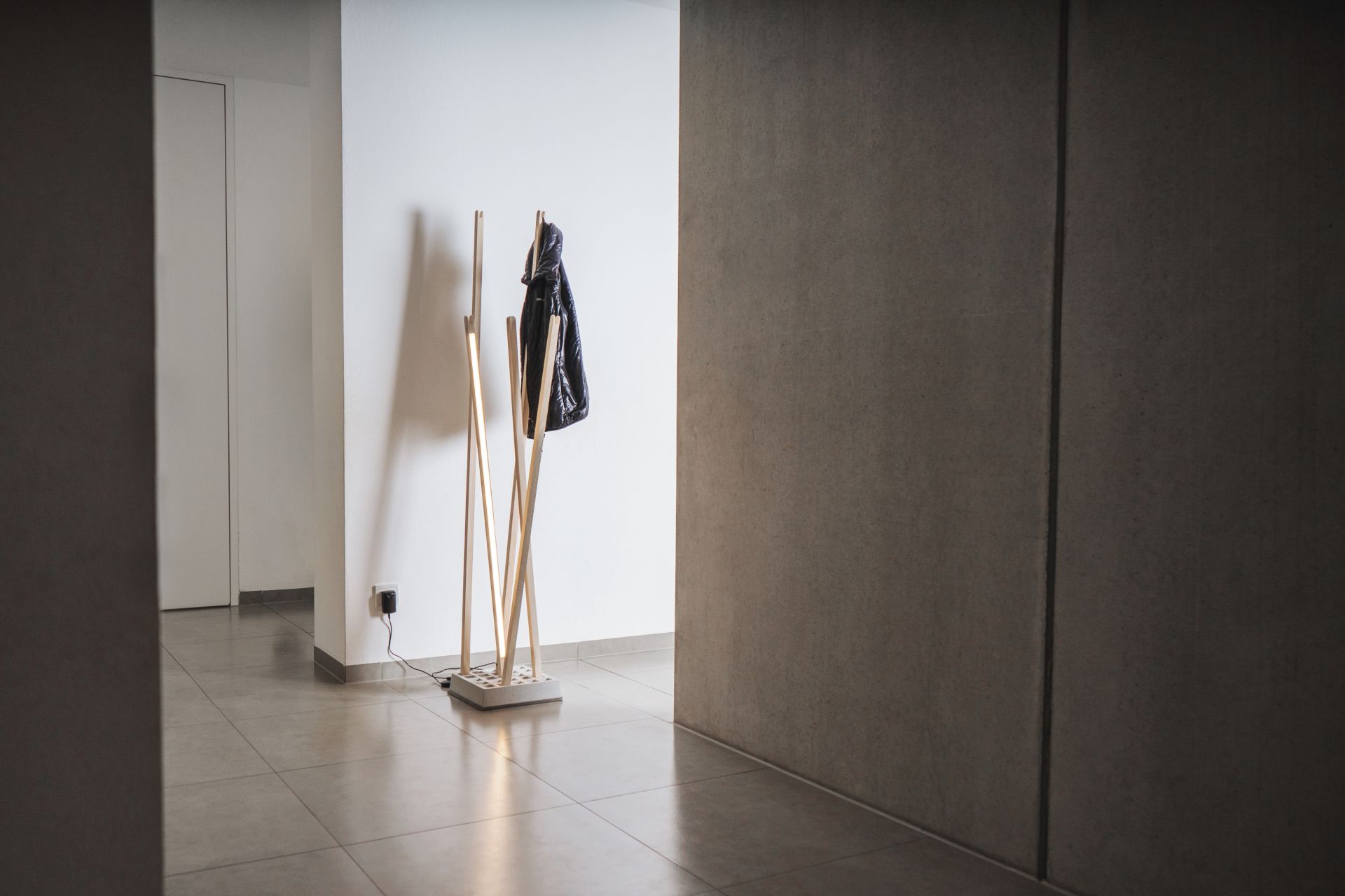 Nils Holger Moormann Pin Coat Garderobe mit Pin Light Leuchte und schwarzer Jacke im Flur.