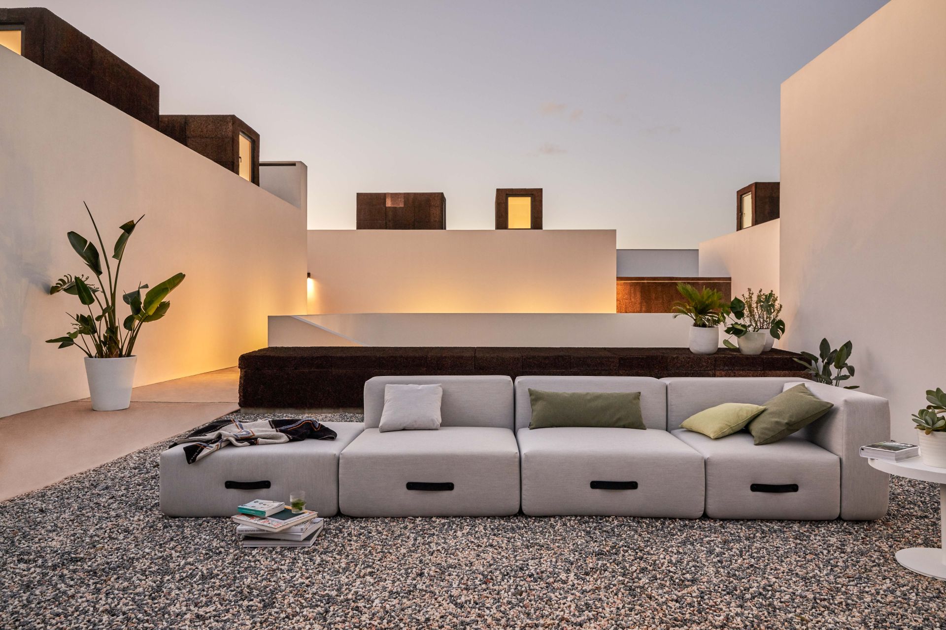 Miami Outdoor Sofa von Conmoto mit Hocker auf Kiesterrasse, minimalistisches Design mit Pflanzen.