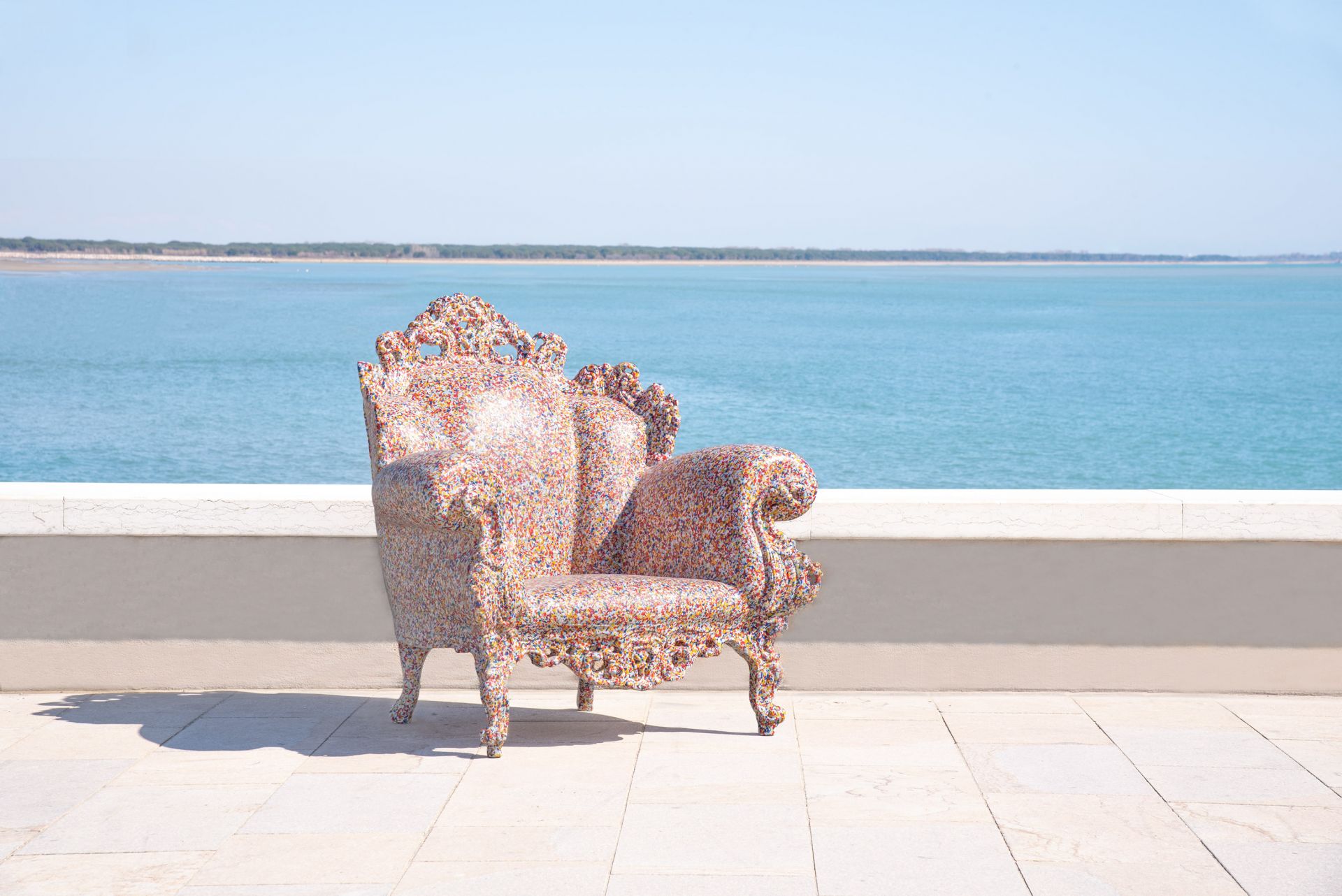 Magis Proust Sessel Outdoor vor Meer, bunter Design Gartenstuhl mit geschwungenen Armlehnen.
