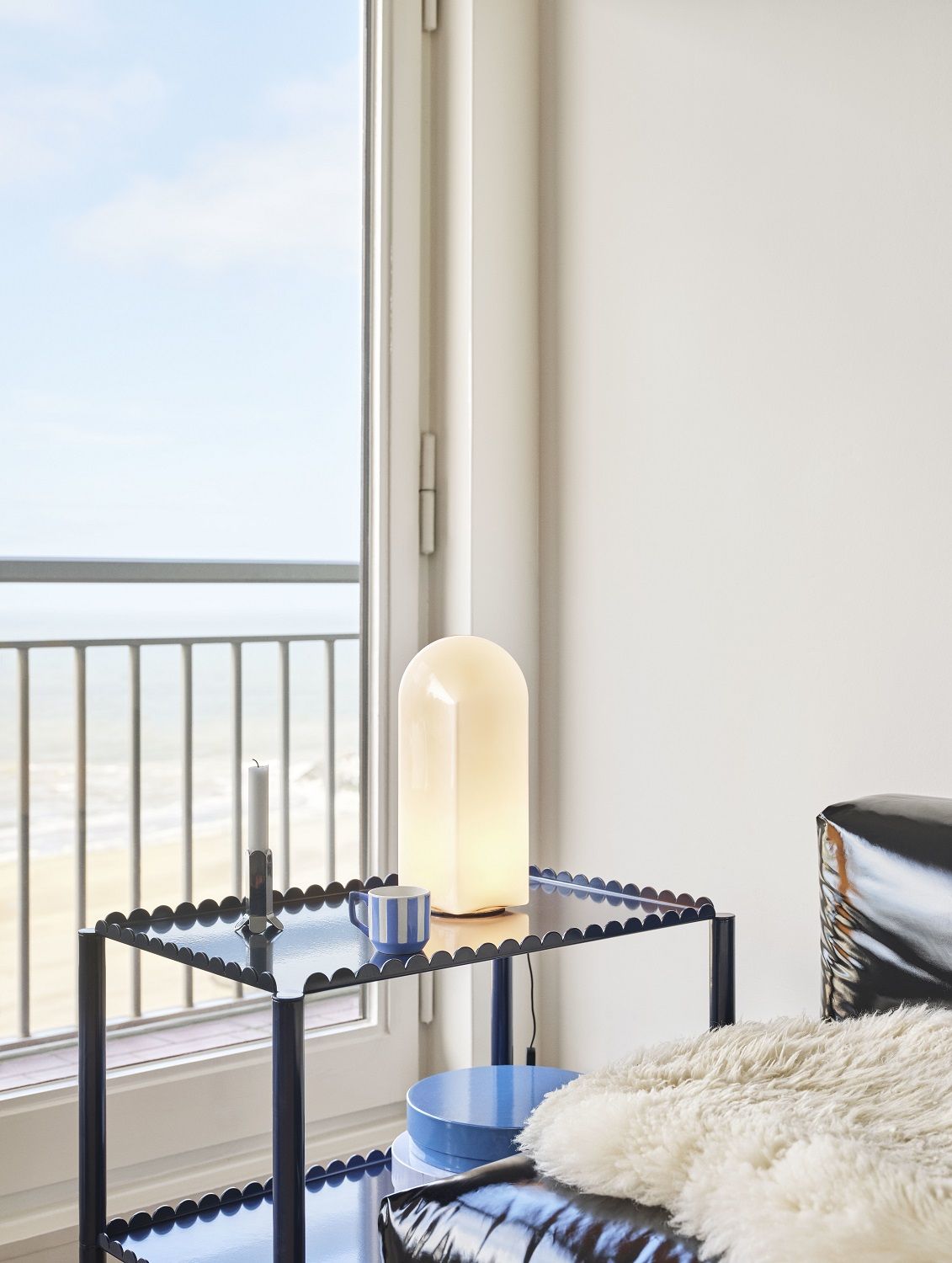 Blauer Arcs Trolley Servierwagen von Hay mit Lampe und Deko vor Fenster mit Meerblick.