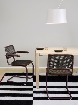 S 64 V Thonet Freischwinger Stühle aus Stahlrohr mit Armlehne und Wiener Geflecht vor Esstisch.