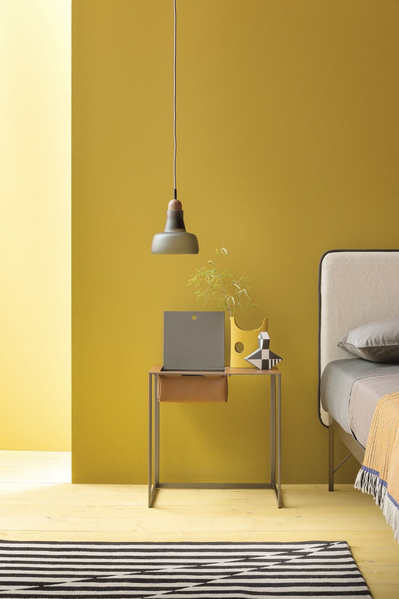 Moderner Taschino Nachttisch von Zanotta mit Schublade, Lampe und Deko-Objekten vor gelber Wand.