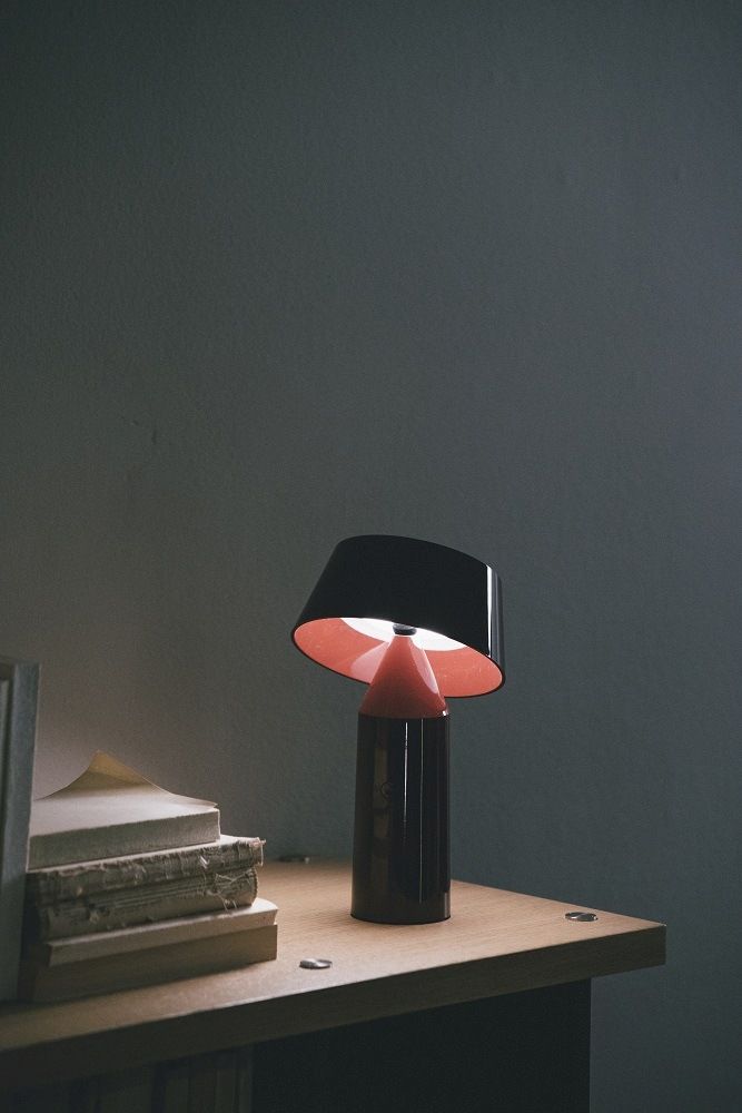 Bicoca Tischleuchte von Marset, rot-schwarze Akkuleuchte auf einem Tisch mit Büchern.