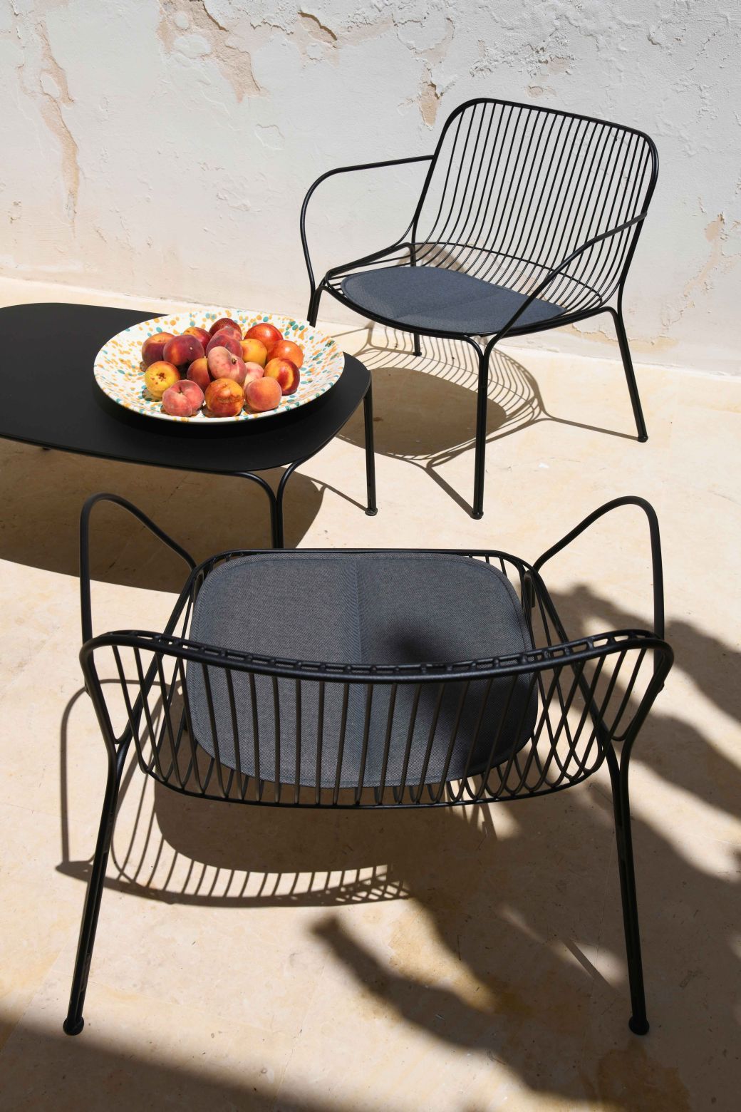 Schwarzer Kartell Hiray Outdoor Kaffeetisch mit Obstschale und zwei passenden Sesseln mit grauen Sitzkissen.