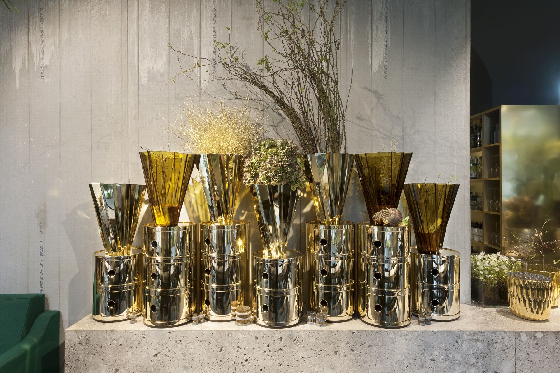 Goldene Componibili 3er Elemente von Kartell, kombiniert mit Vasen und floralen Elementen auf einer Ablage.