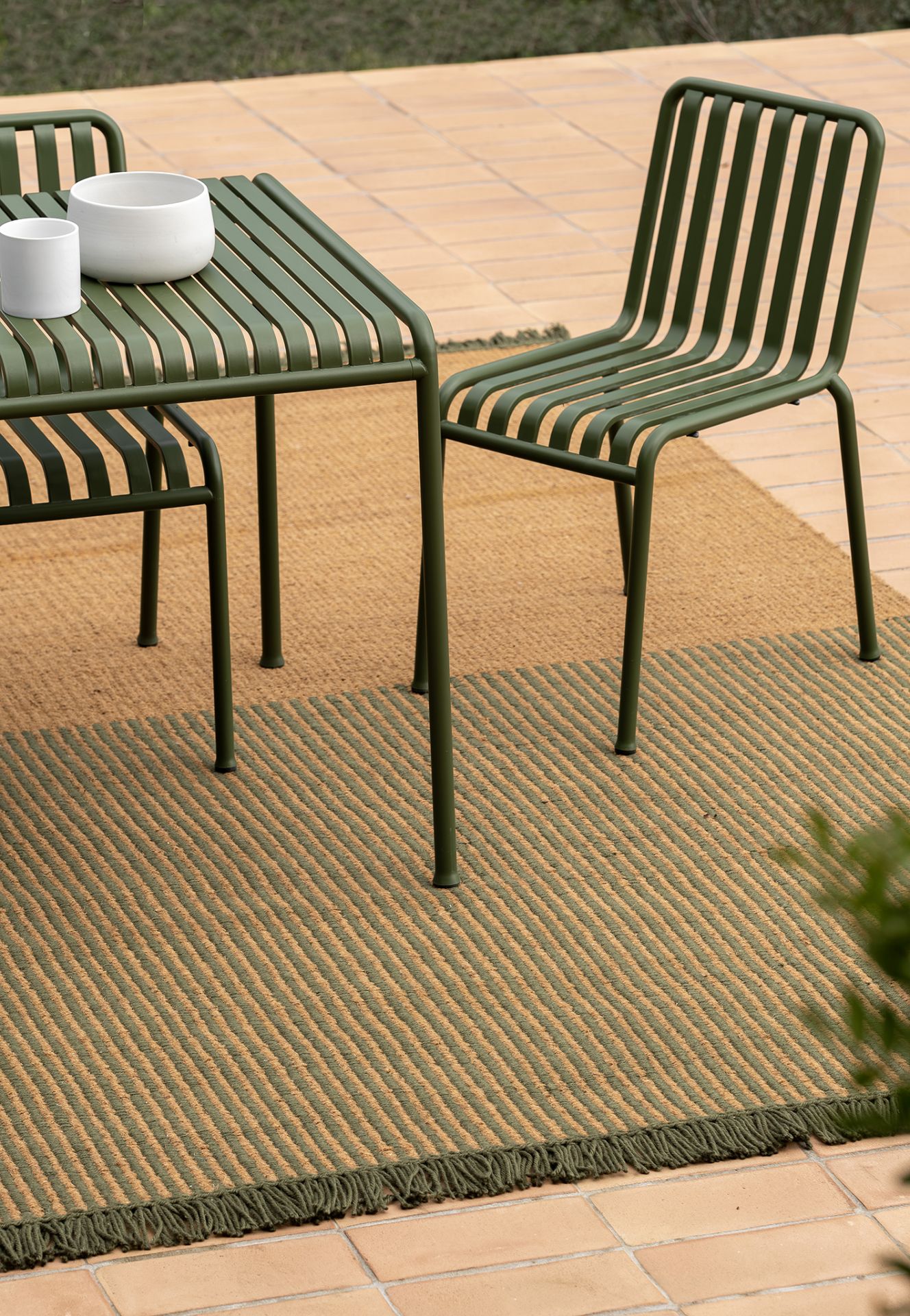 Nanimarquina Outdoor Teppich im Garten mit grünen Streifen und passendem Gartentisch mit Stühlen.