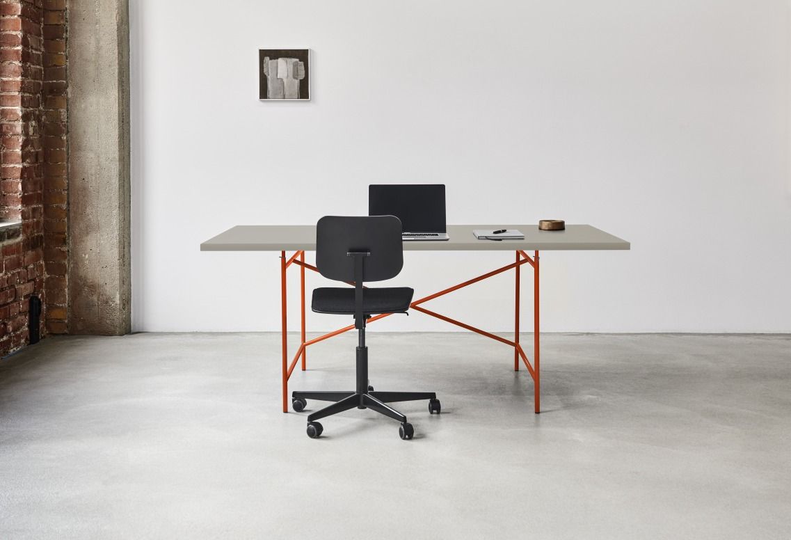 Eiermann Tisch mit orangefarbenem Gestell, grauer Tischplatte, Bürostuhl, Laptop und Notizbuch in modernem Büro.